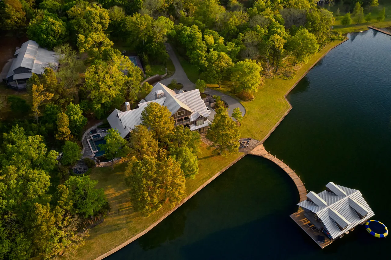 Aerial view of a lakeside residence featuring a metal roof and a boat dock with a covered seating area.