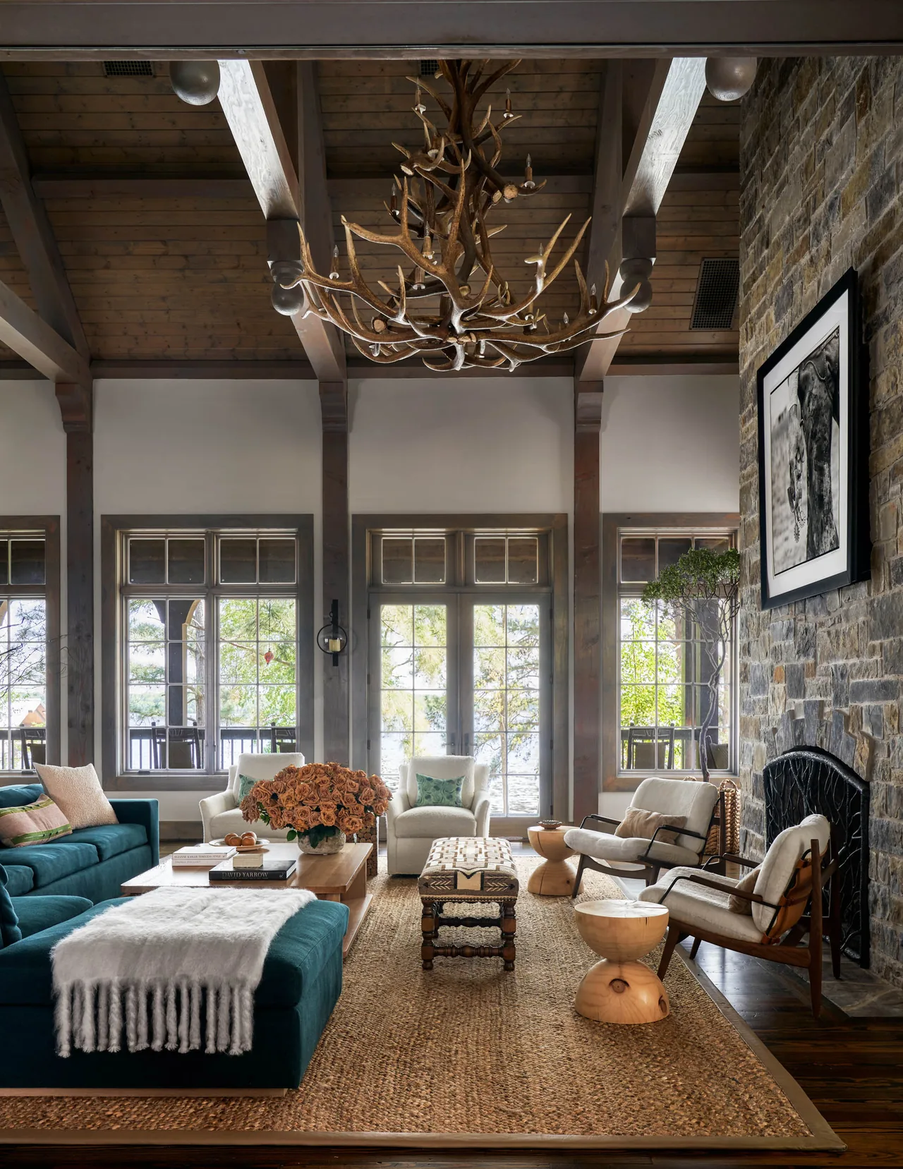 Living room featuring a vaulted wood ceiling, large stone fireplace, and an antler chandelier with lake views.