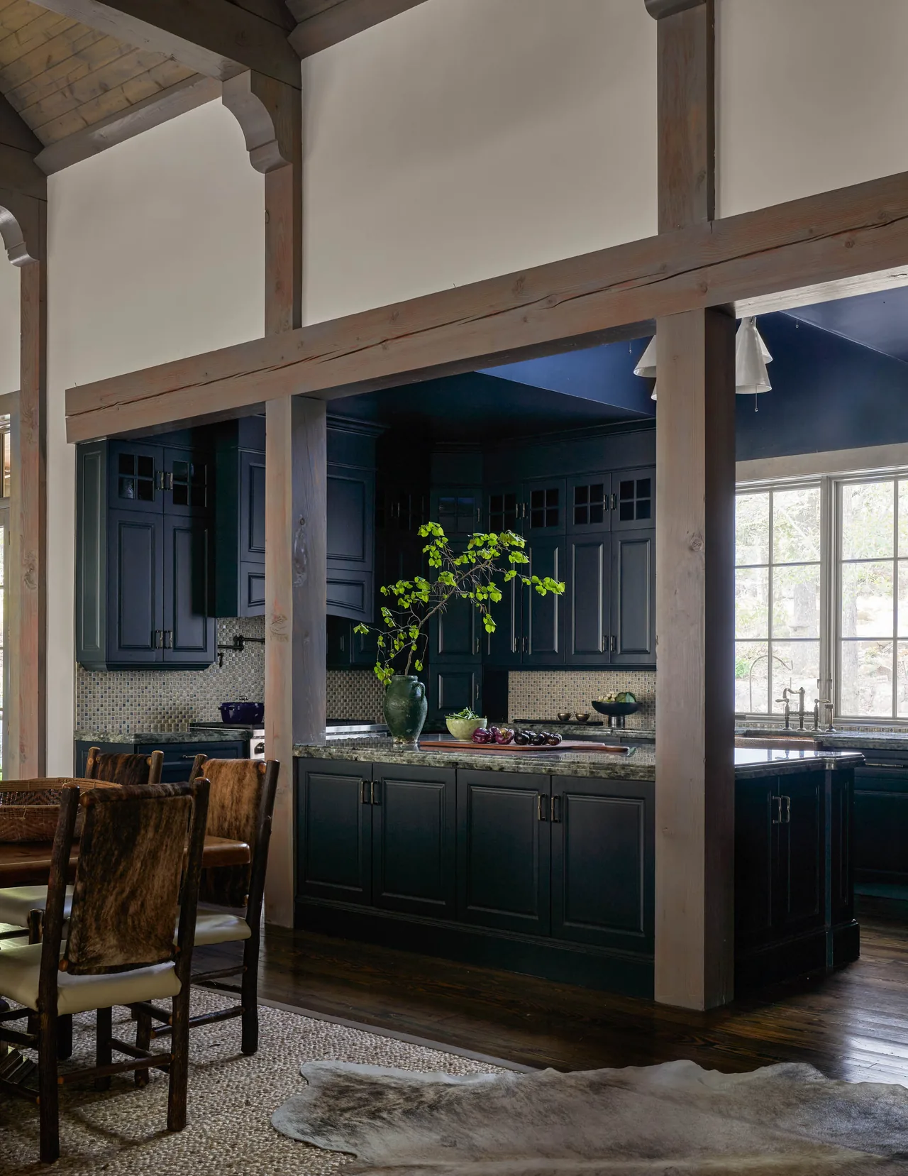 Kitchen with dark cabinetry and island adjacent to dining area under a vaulted wooden ceiling.