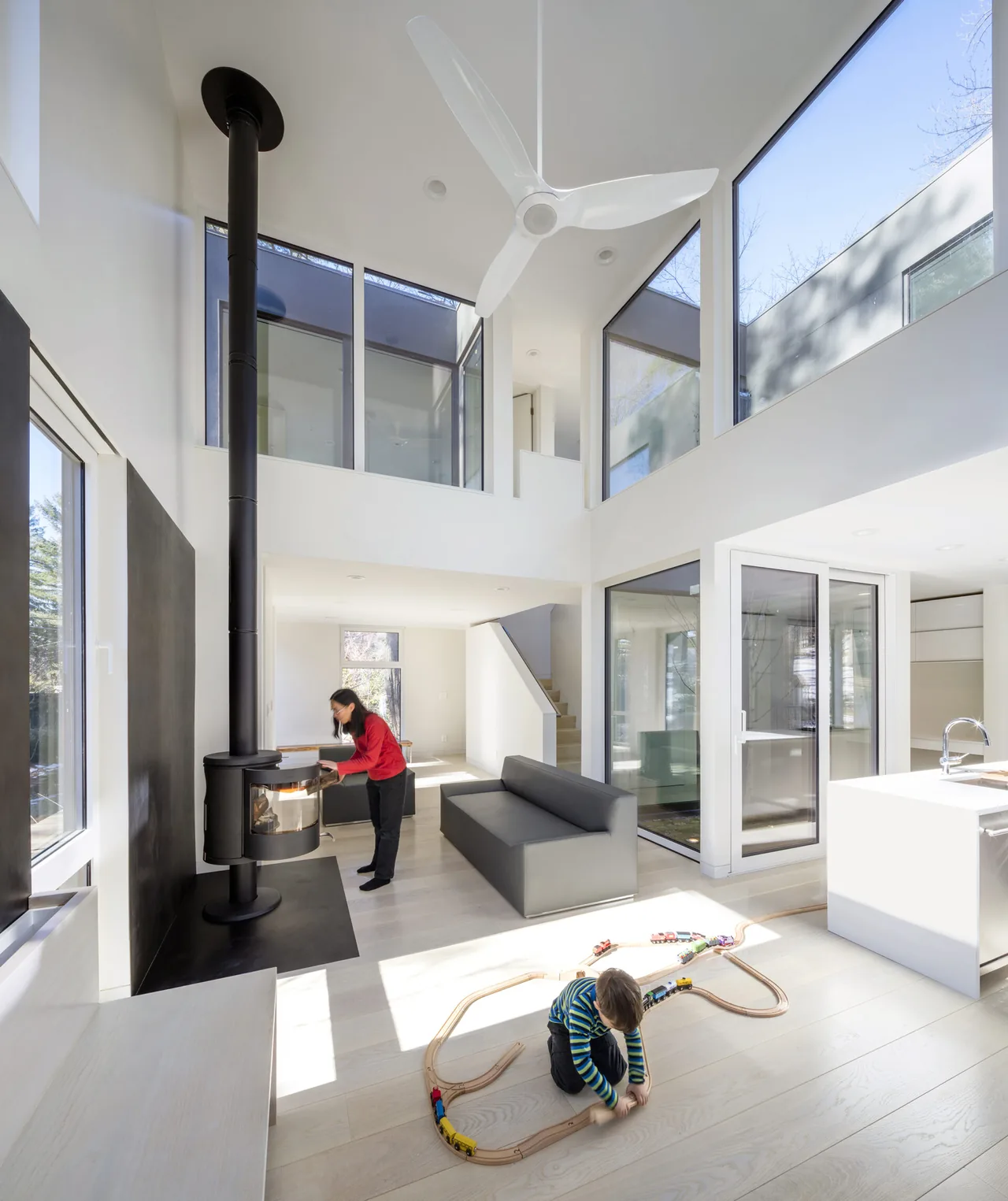 Interior of Grow Box features a double-height living area with floor-to-ceiling windows, a suspended wood stove, and minimalist black couch.