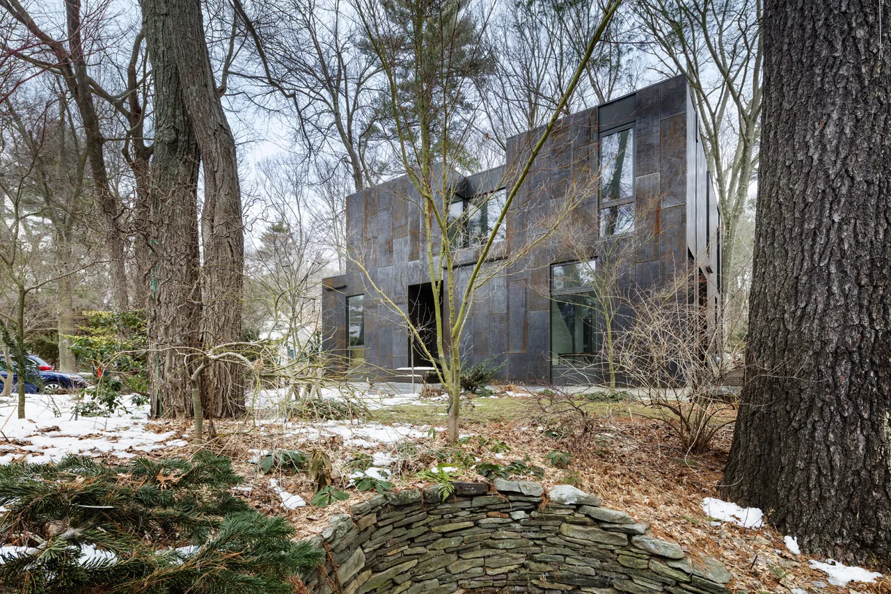 Cube-shaped modern house with weathered steel exterior walls in a wooded winter setting.