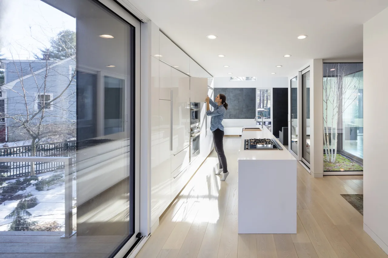 Bright modern kitchen with white cabinetry, kitchen island with cooktop, and large glass doors opening to outdoors.