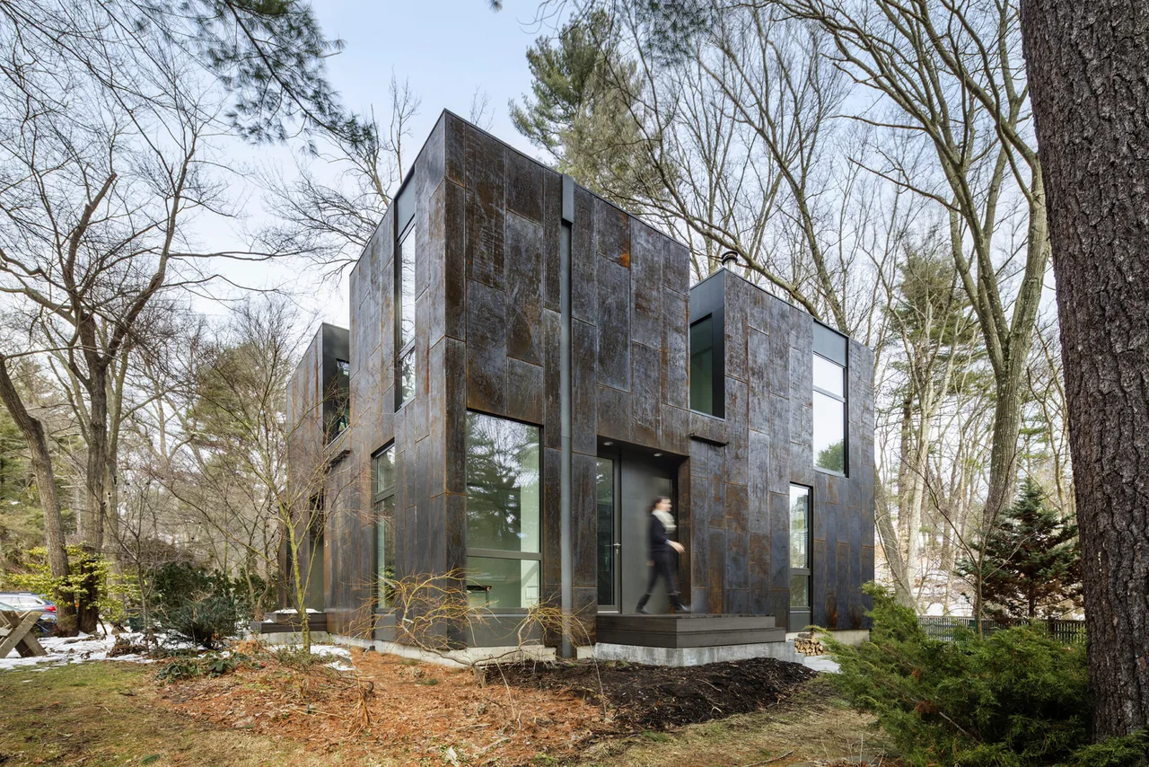 The Grow Box project by Merge Architects features a modern house clad in rusted metal panels set in a wooded landscape.