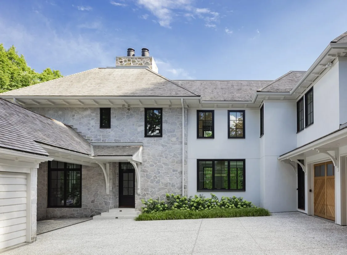 Birchwood Terrace exterior features a blend of stone and stucco walls, black window frames, and wood garage doors by LDa Architecture & Interiors.
