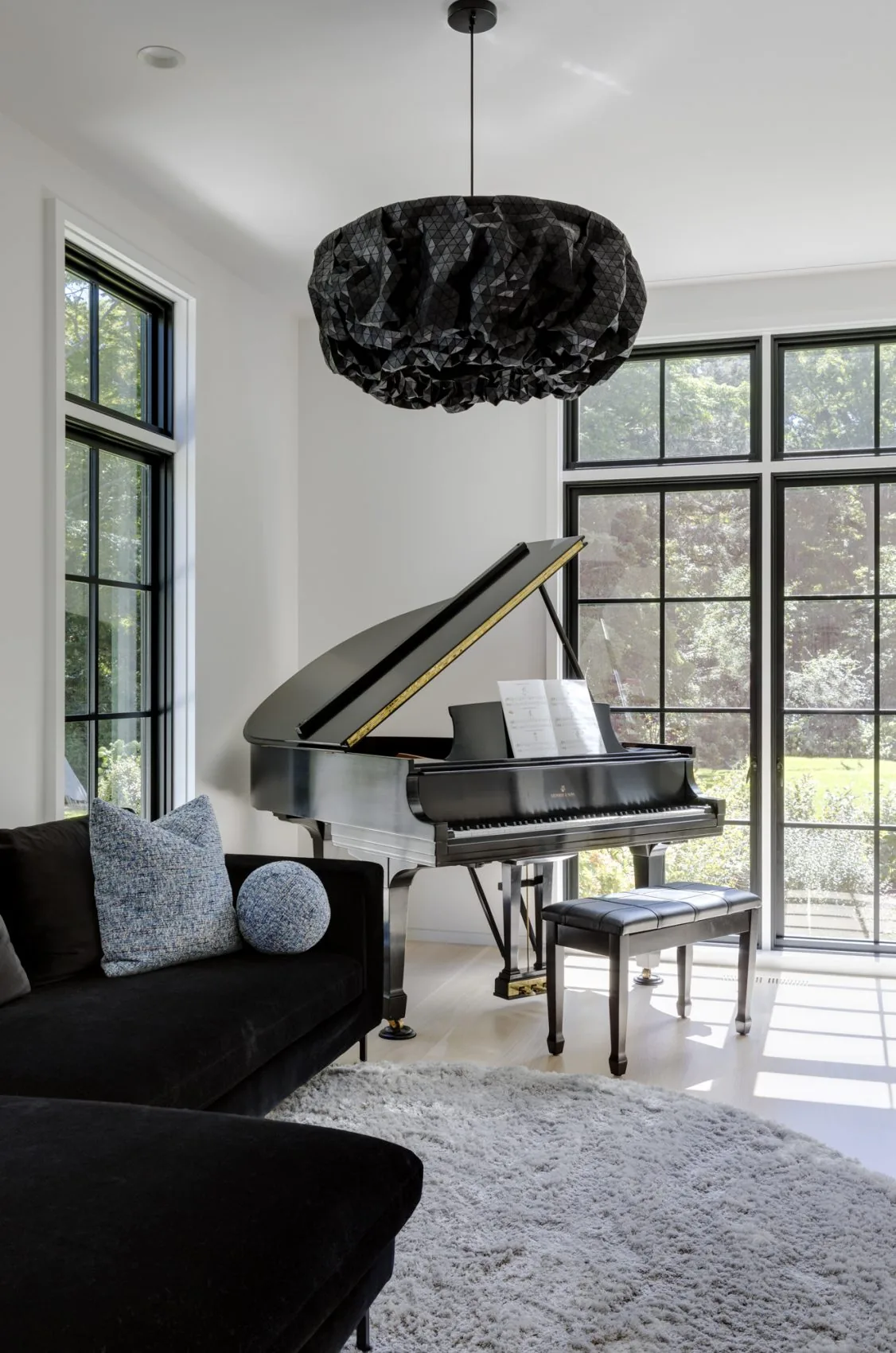 Living room featuring a black grand piano and large black-framed windows allowing abundant natural light.