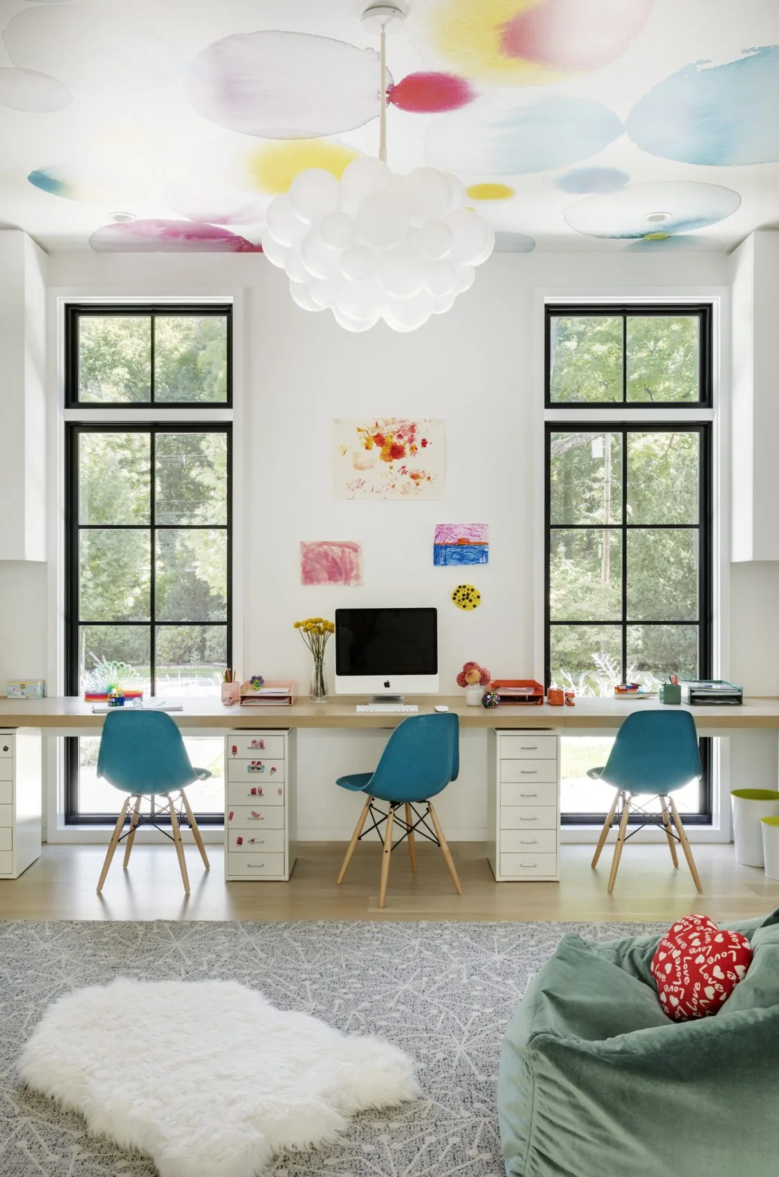 Home office with a triple workstation, black grid windows, and a playful ceiling light fixture.