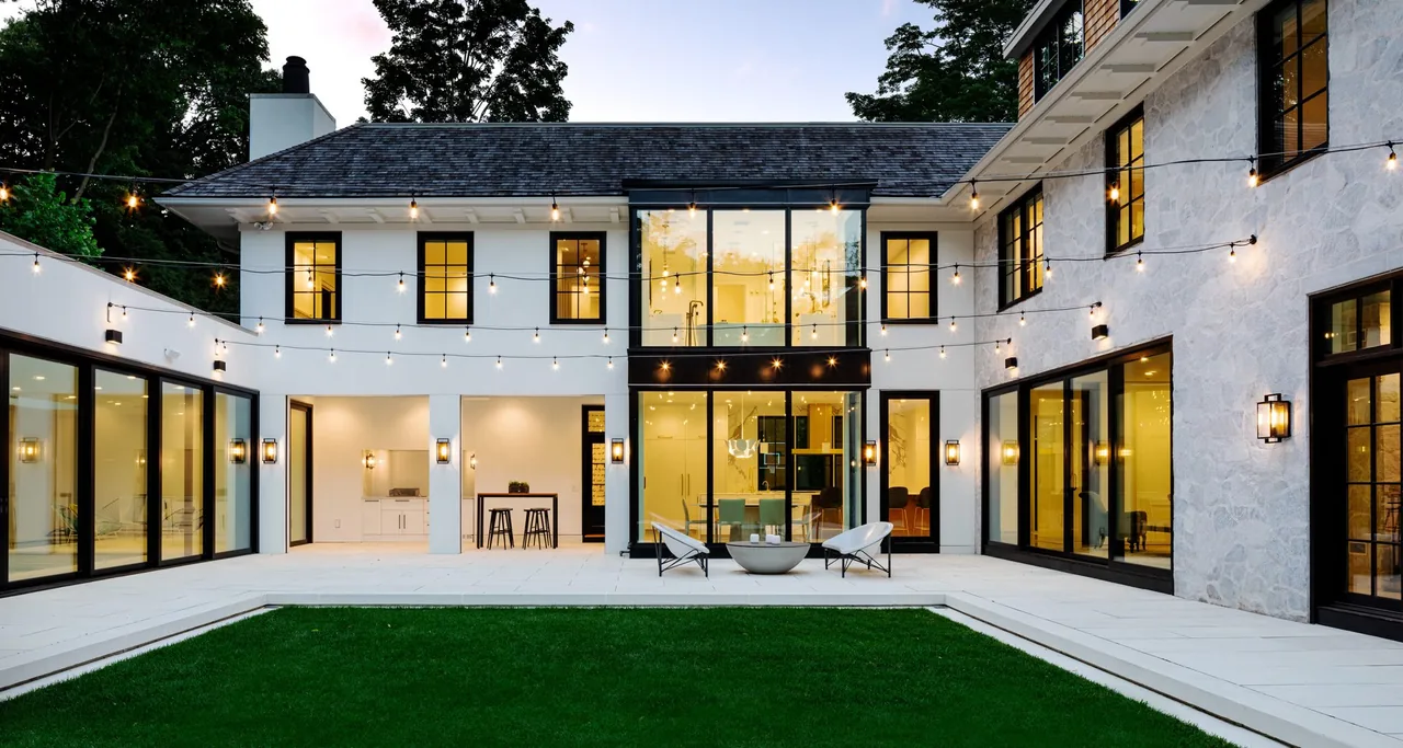 Exterior rear of Birchwood Terrace showing white walls with stone accents, black window frames, and string lights over patio and lawn.