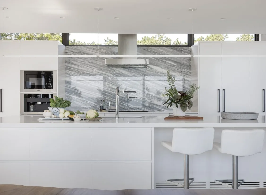 Modern kitchen with white cabinetry, marble backsplash, and clerestory windows, featuring a stainless steel range hood.