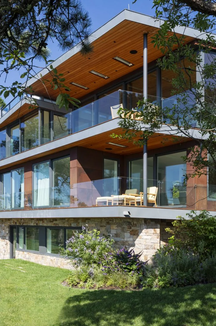 Miter Point modern home features glass balconies and wood soffits with a stone exterior base.