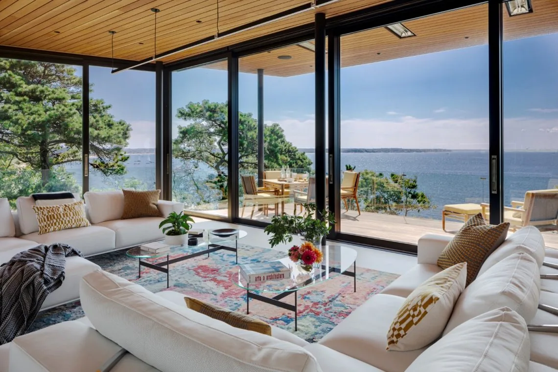 Living space with floor-to-ceiling glass doors overlooking a waterfront deck and landscape.