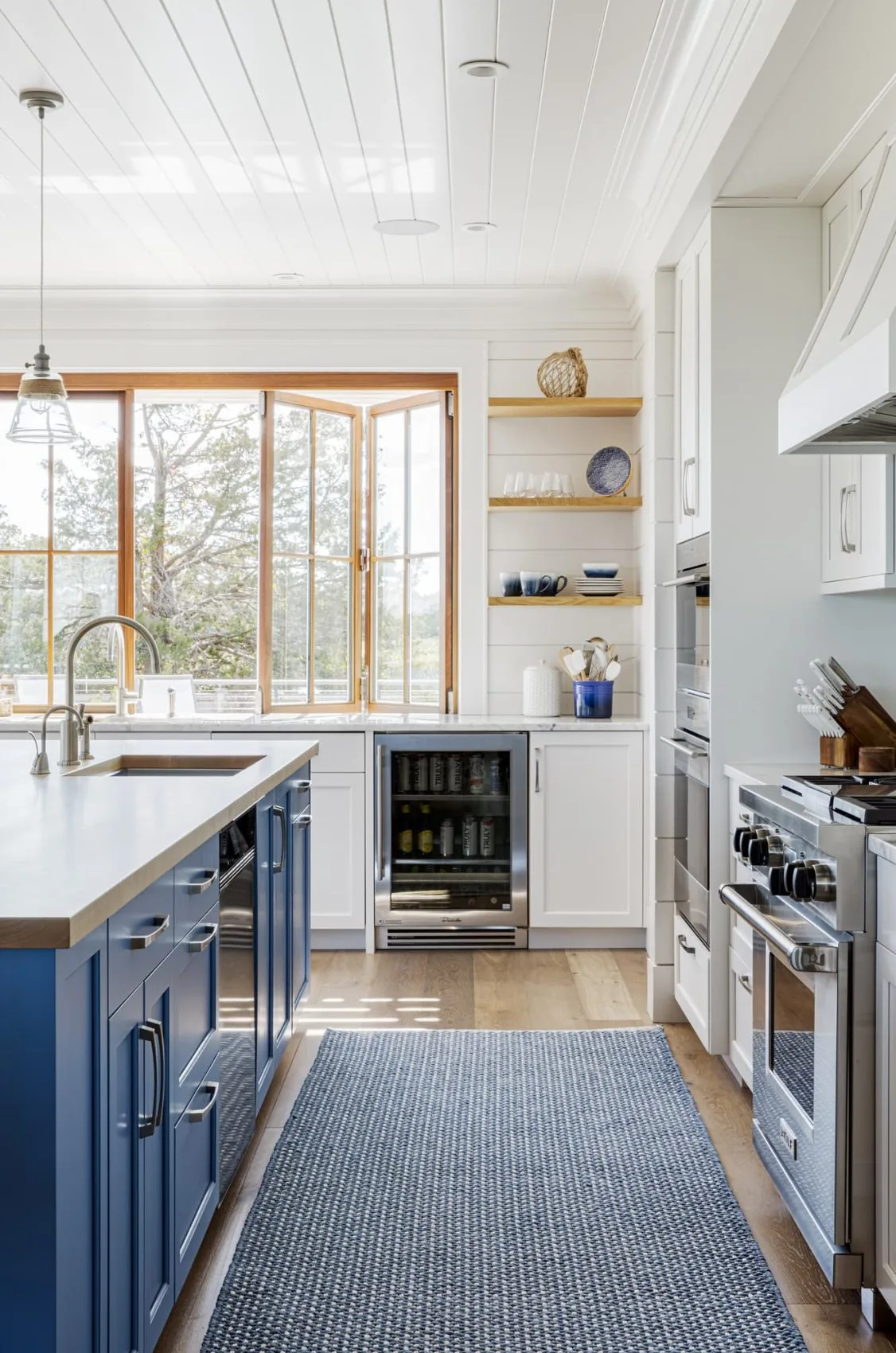 Kitchen with blue cabinetry island, stainless appliances, wooden open shelves, and white countertops from Salten Point project.