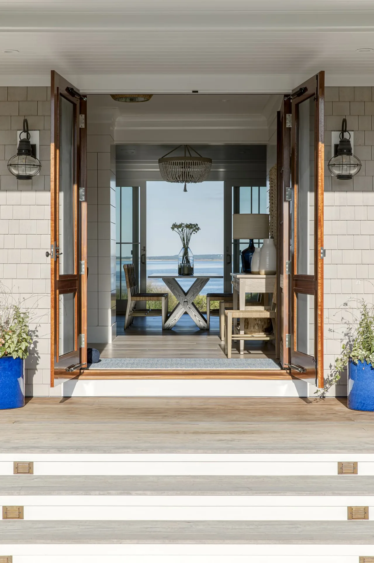Open wooden doors lead to a dining area with a chandelier and waterfront views in the Salten Point project.