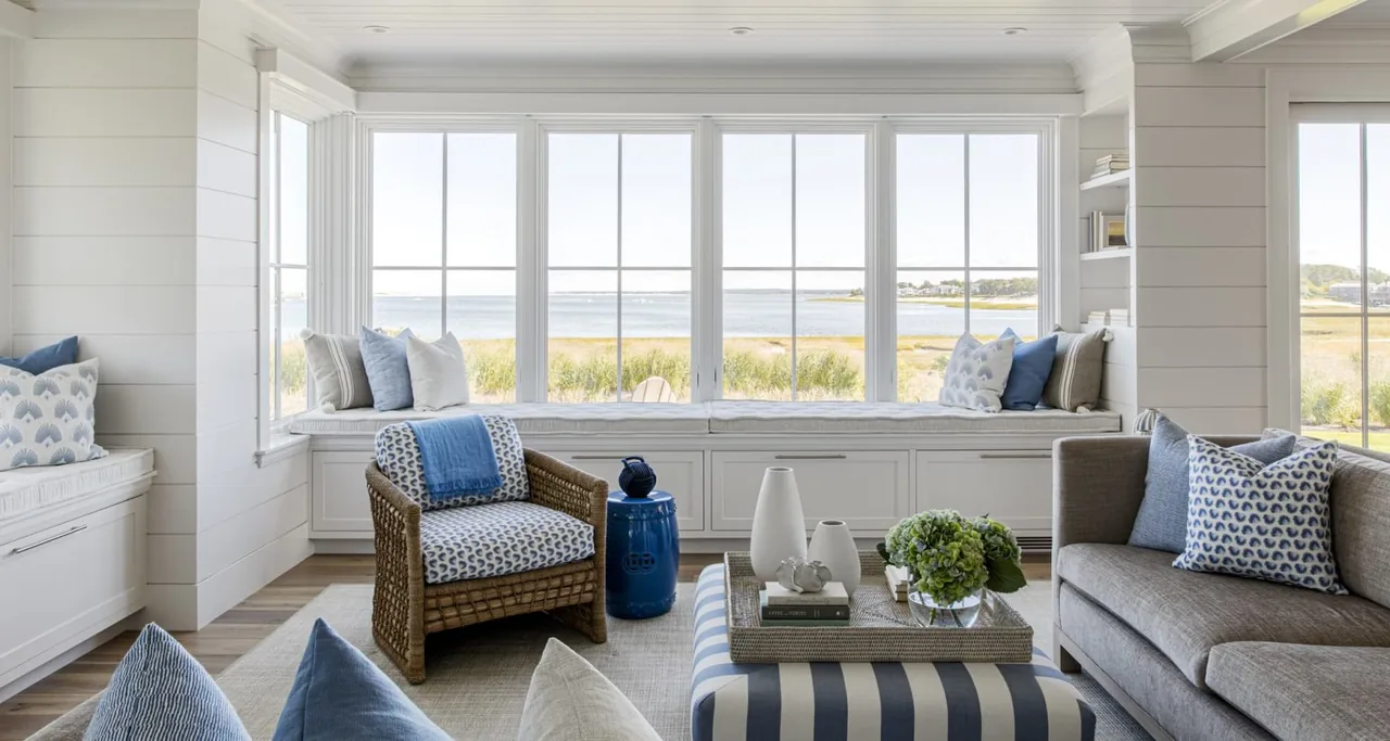 Living room features large picture windows overlooking water and built-in window seats with cushions.