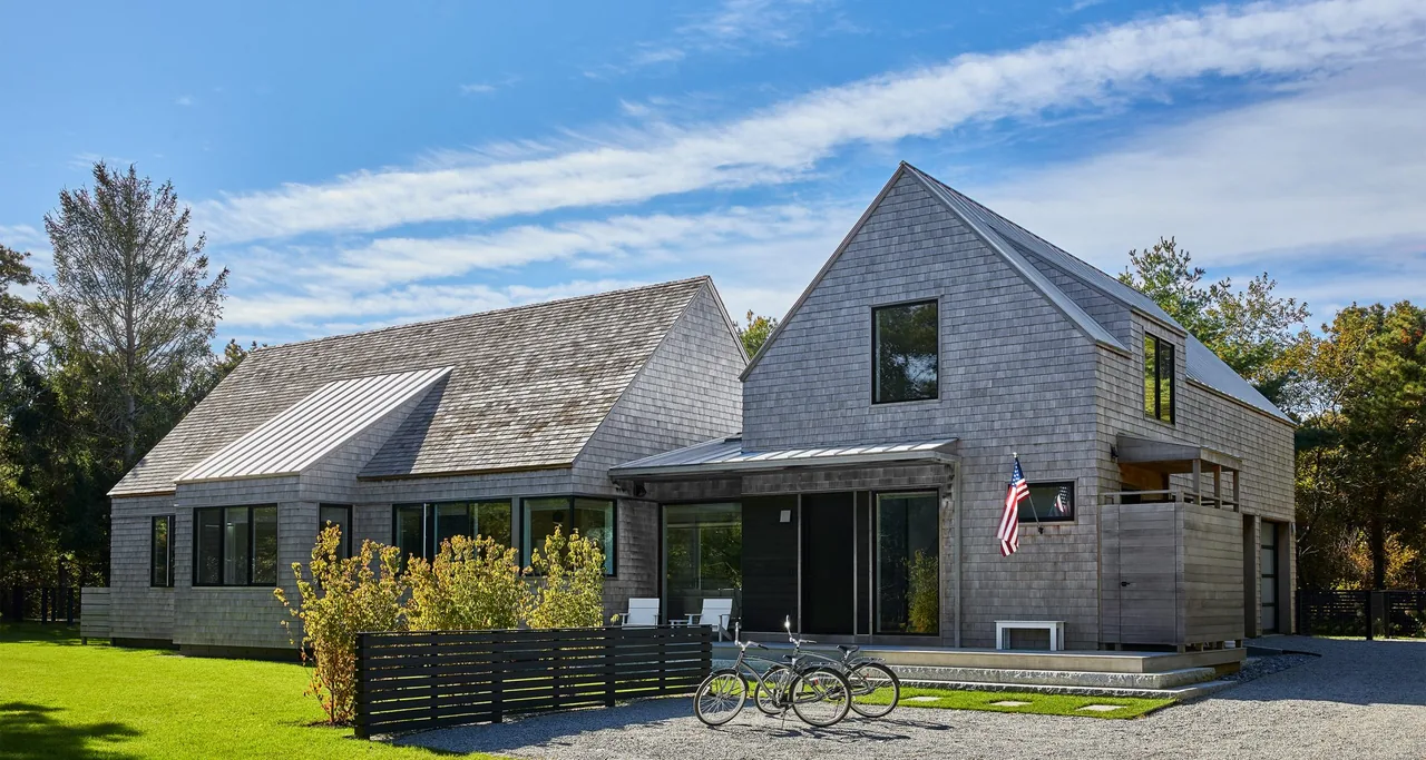 Two connected residential buildings with wood shingle siding and gable roofs under a blue sky.