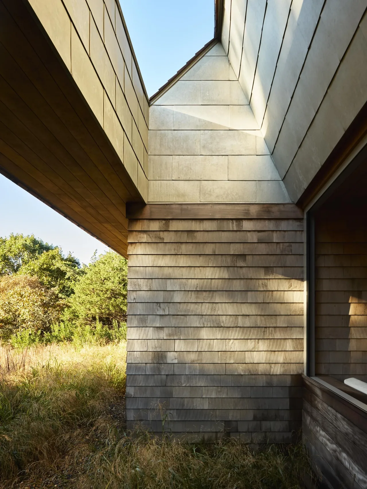 Close-up view of the Wink House's exterior corner clad in wood shingles with natural landscaping around it.