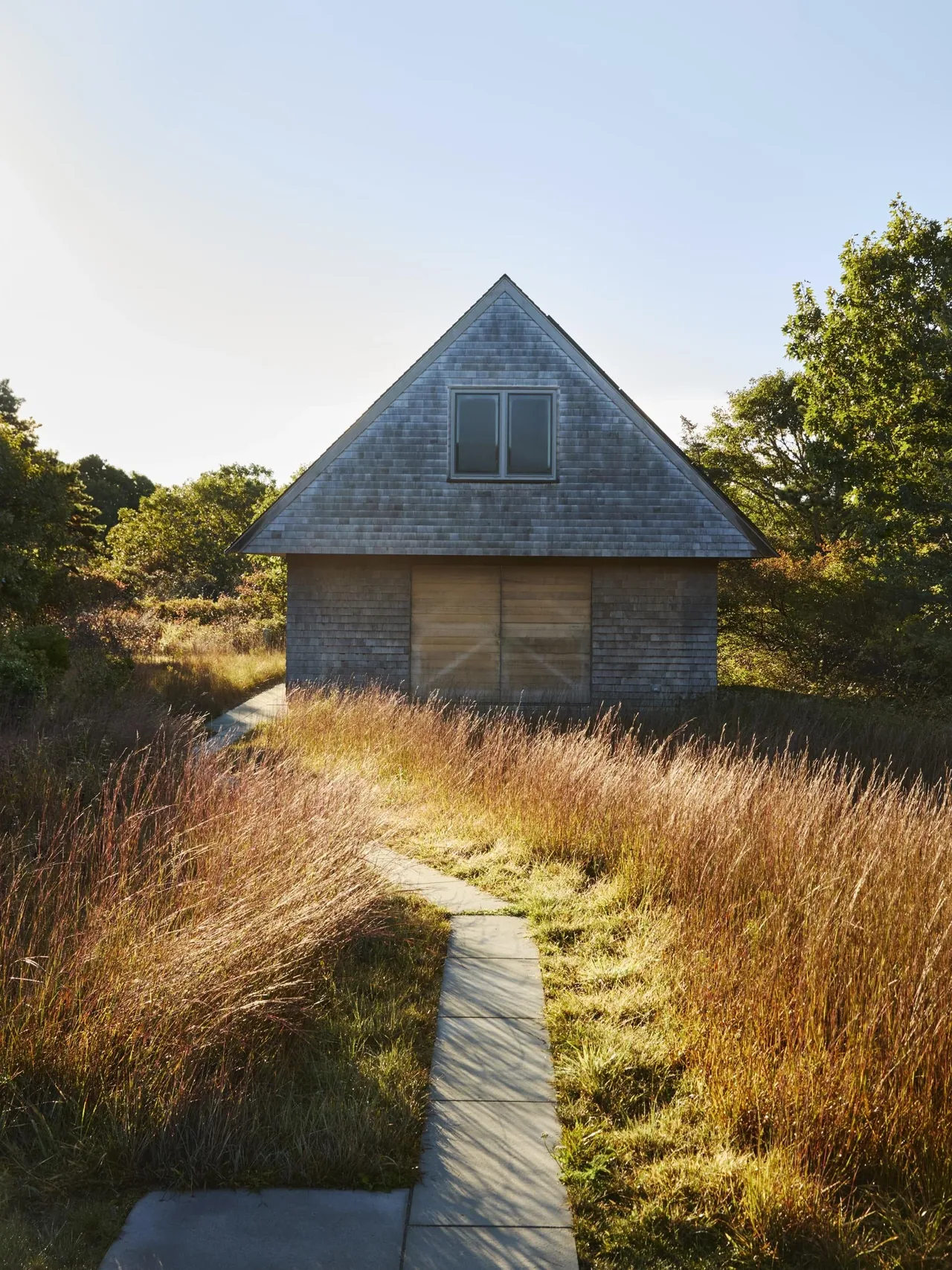 Wink House features gray shingle siding, a pitched roof, and a dormer window, set amid natural landscaping in Boston.