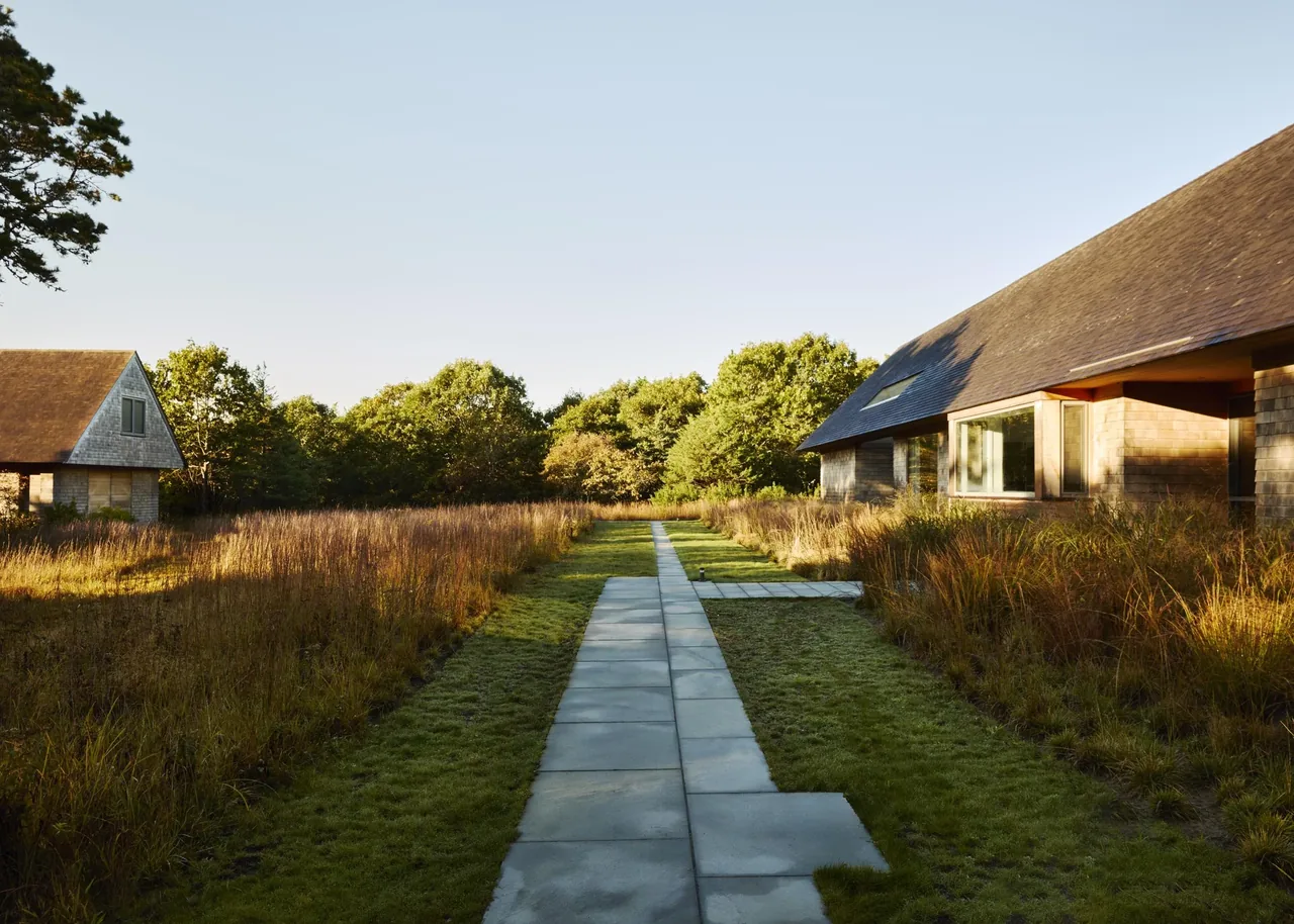 The Wink House features shingle siding and a stone walkway amid natural landscaping by Noury-Ello Architects.
