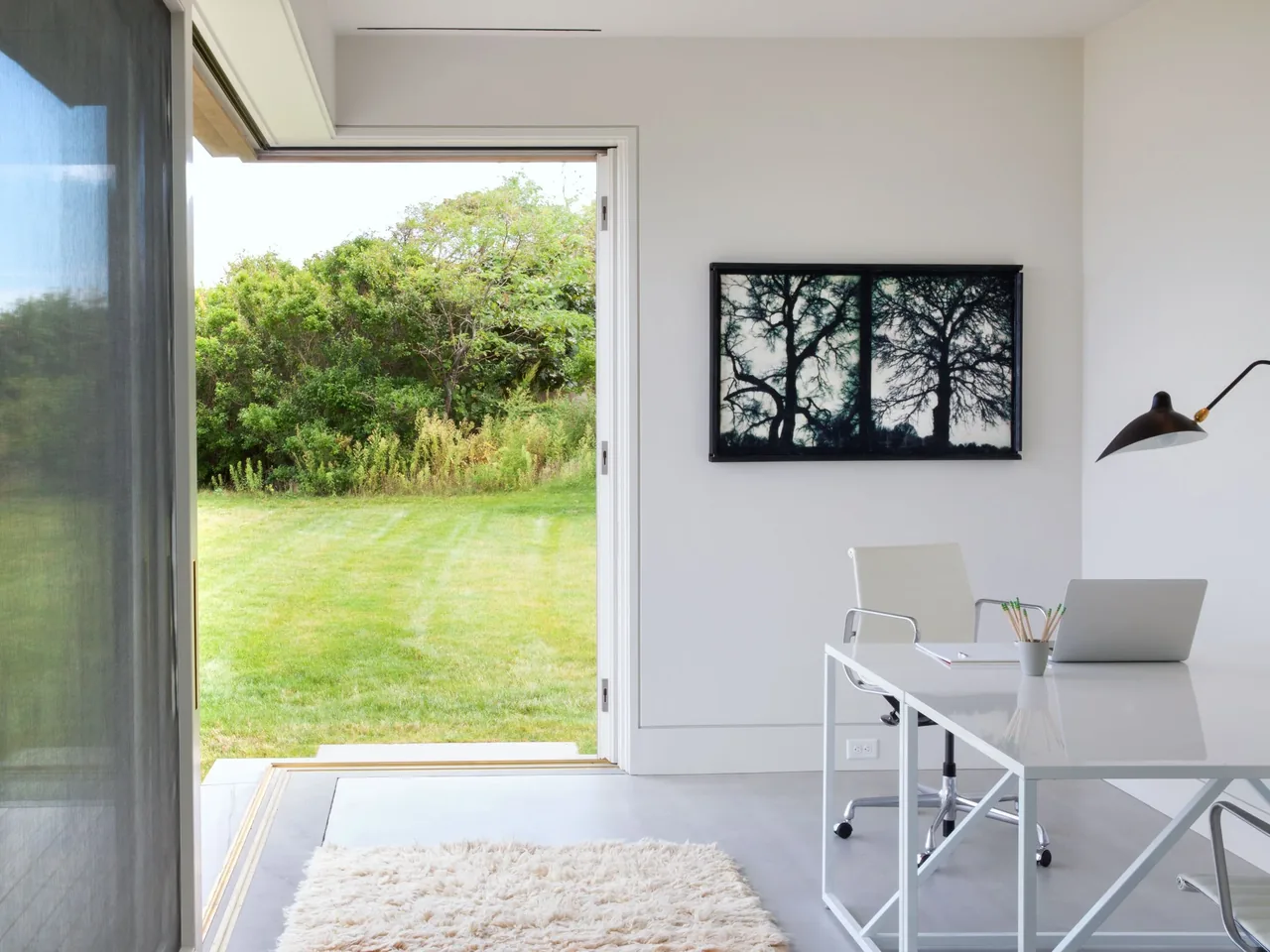 Island House office features minimalist design with a white desk and large open doorway to a green yard.