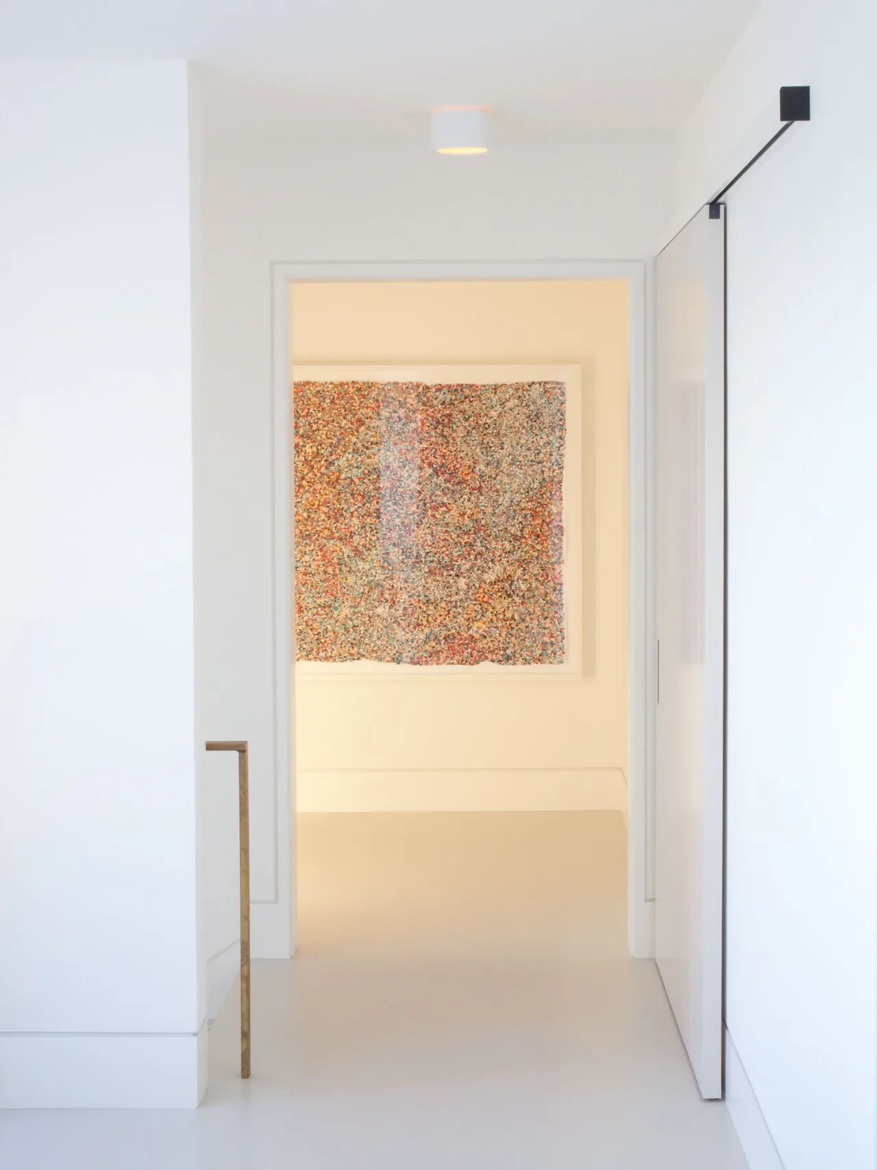 Minimalist white hallway with a large colorful abstract artwork framed on an interior wall.