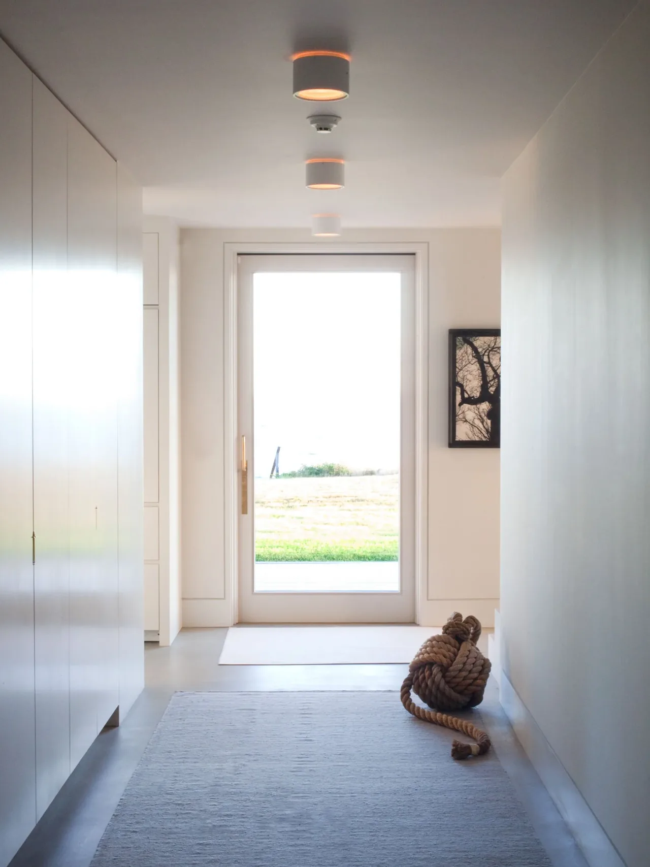 A bright hallway features recessed lighting and a glass door with a view of the yard at Island House.