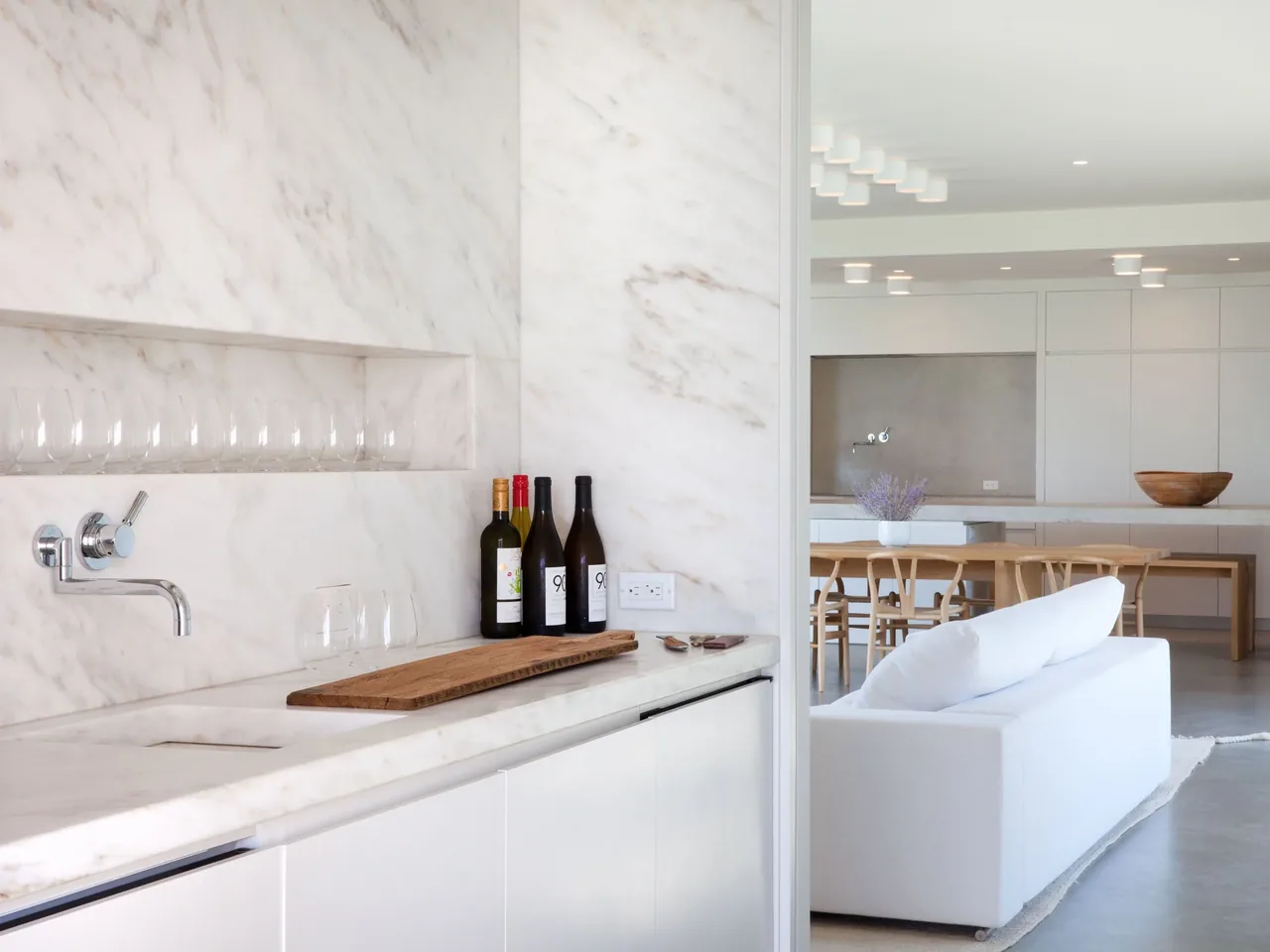 Kitchen wet bar area with marble surfaces and an adjacent dining space featuring natural wood chairs and table.
