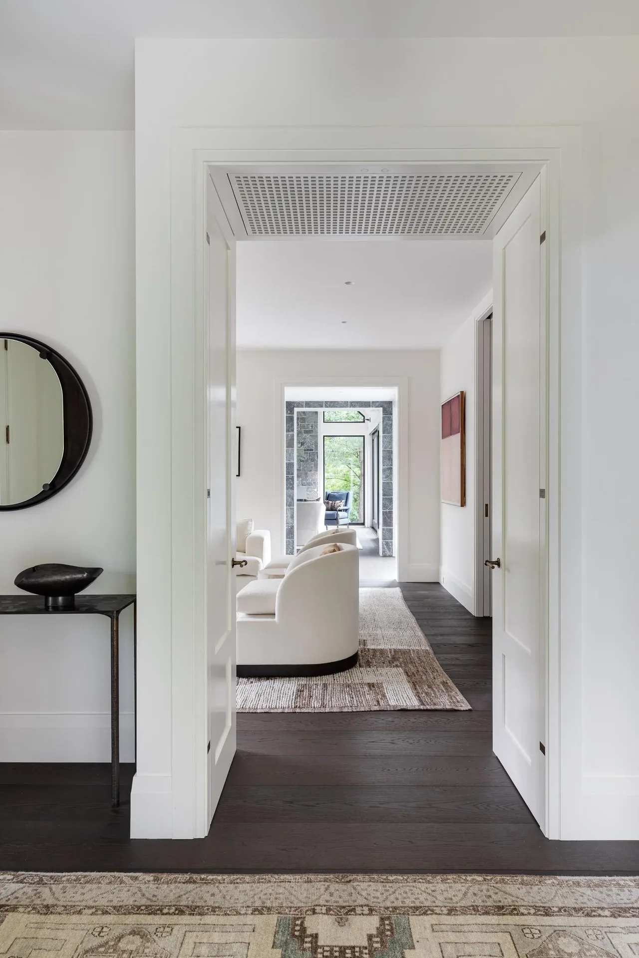 Interior view of a living room with white armchairs, dark wood flooring, and a decorative rug.
