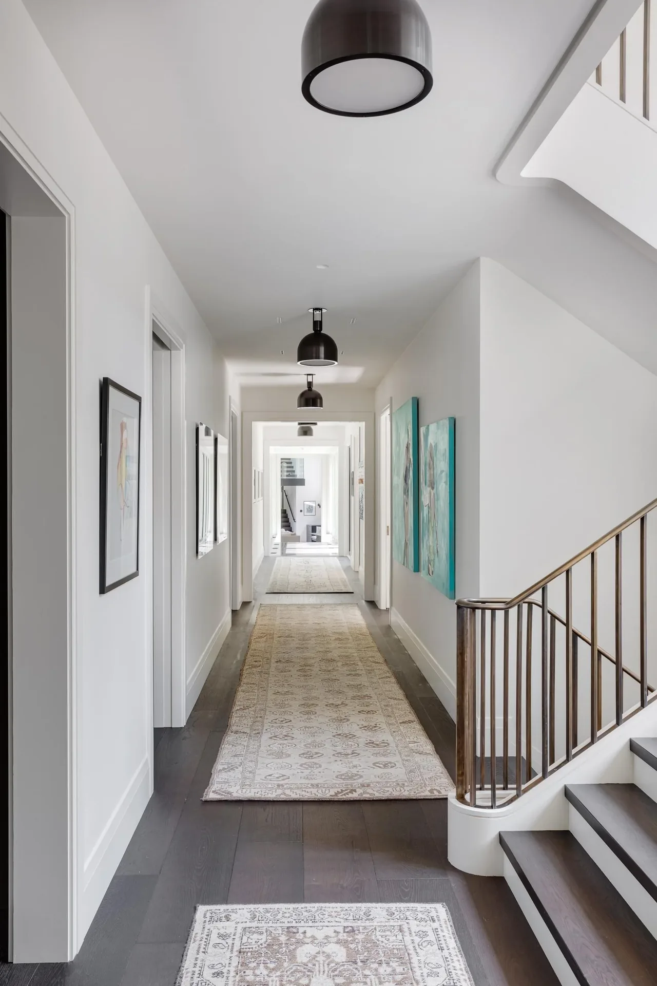 Bright hallway with white walls, artwork, dark wood flooring, and black pendant lighting in Carriage House project.