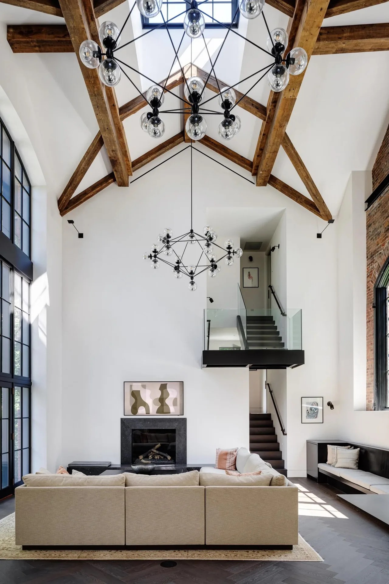 Living room features vaulted ceiling with exposed beams and large black-framed windows in a Carriage House by Noury-Ello Architects.