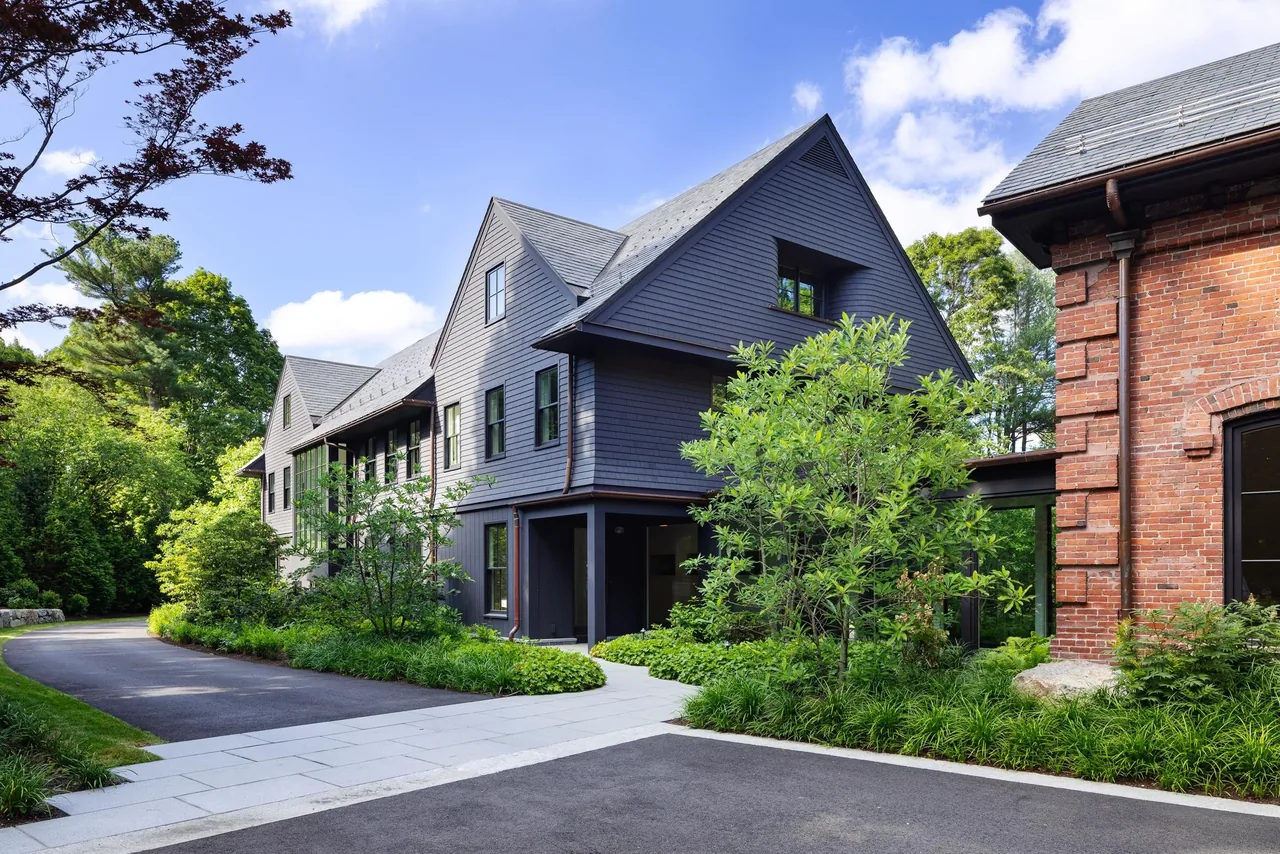 The Carriage House features dark gray wood siding with steep gable roofs next to a traditional red brick structure.