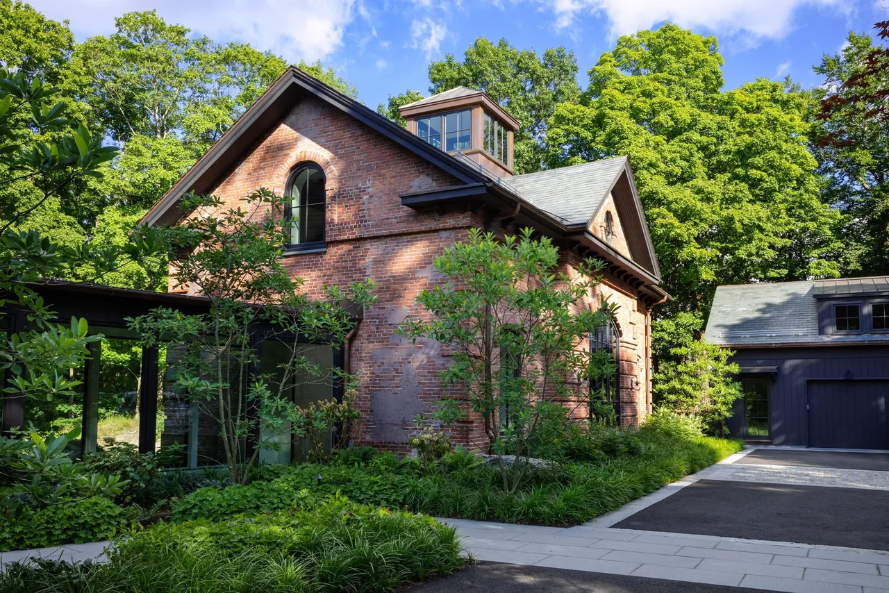 Brick carriage house with tall arched window, dormer window, and landscaped garden near paved driveway in Boston.