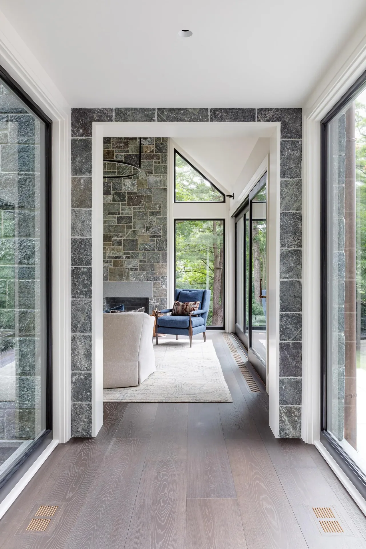Stone-framed hallway leads to a living room featuring a stone fireplace and large triangular window overlooking greenery.