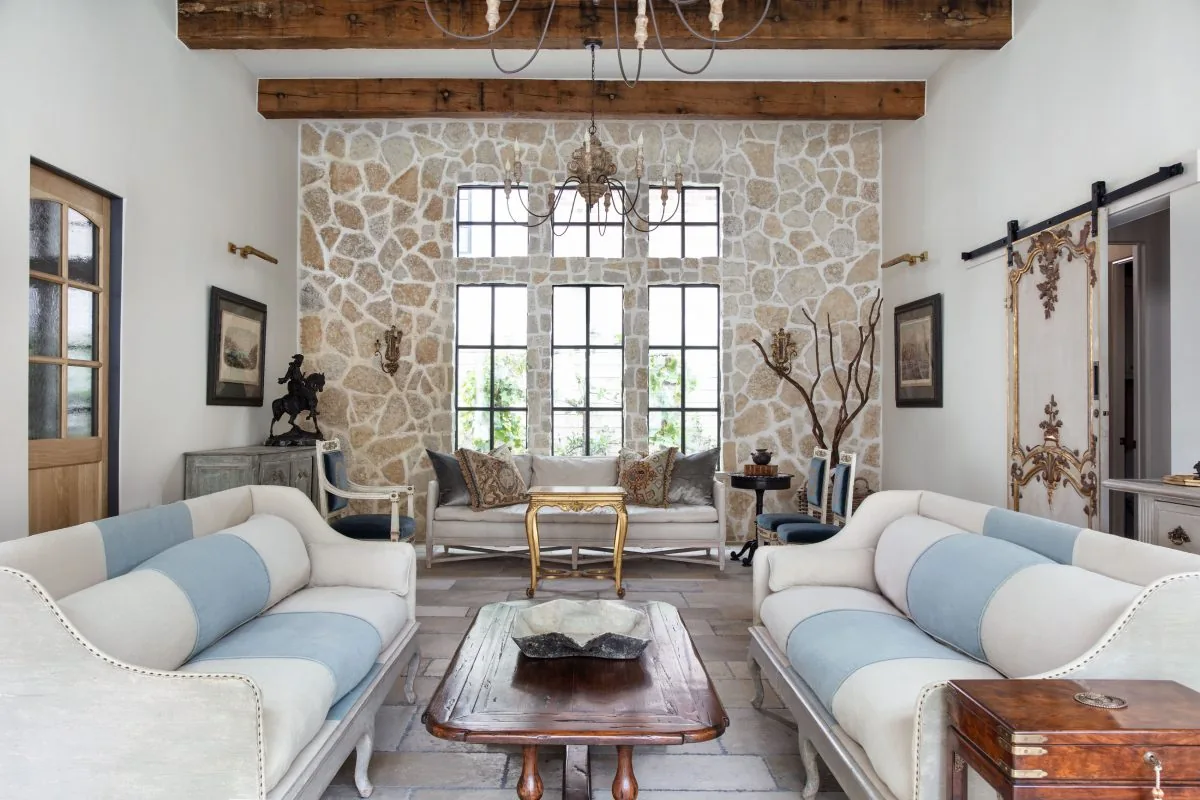 Living room features a stone wall with multiple grid windows, antique-style sofas, and exposed wooden beams.