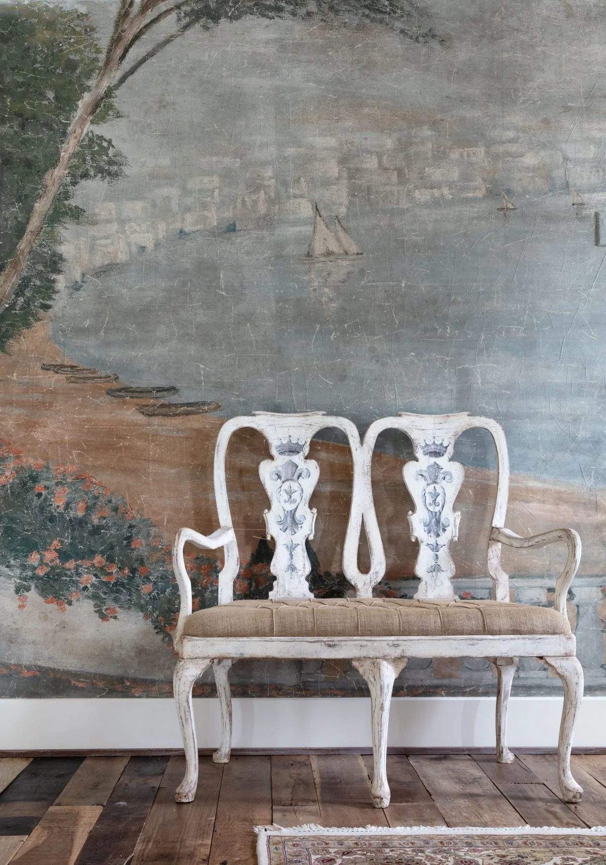 An antique two-seat bench in front of a serene coastal mural painting in the Old-World French Estate project