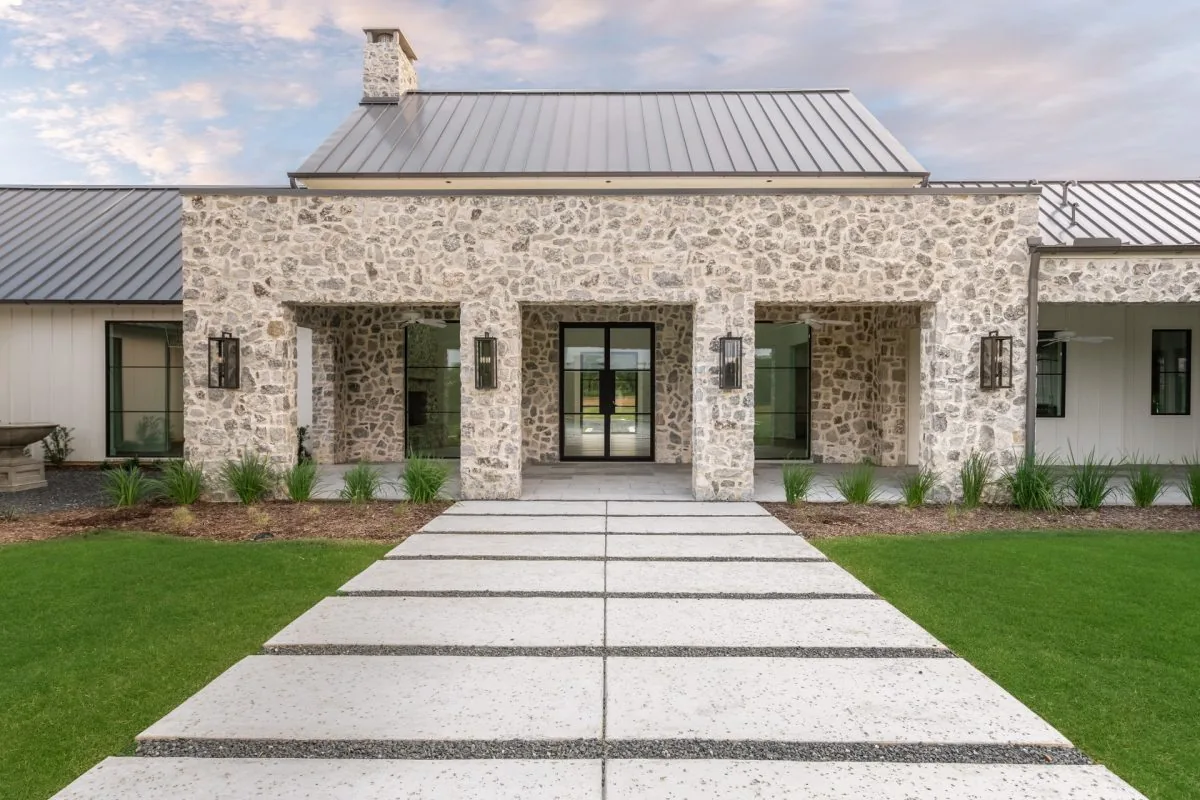 Hill Country Estate features a stone exterior, metal roof, and a symmetrical entryway with black-framed glass doors.