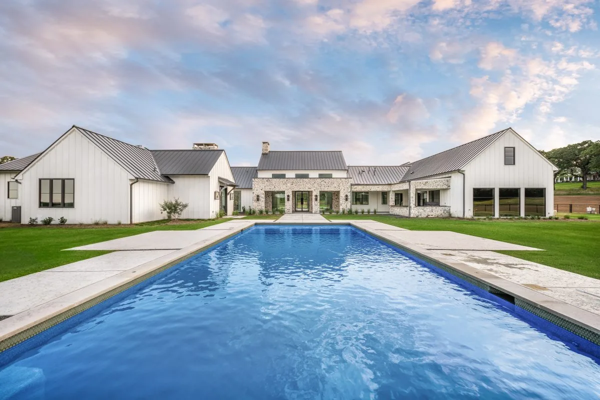Hill Country Estate features a metal roof and stone accents, viewed here from the rear with a pool in front.