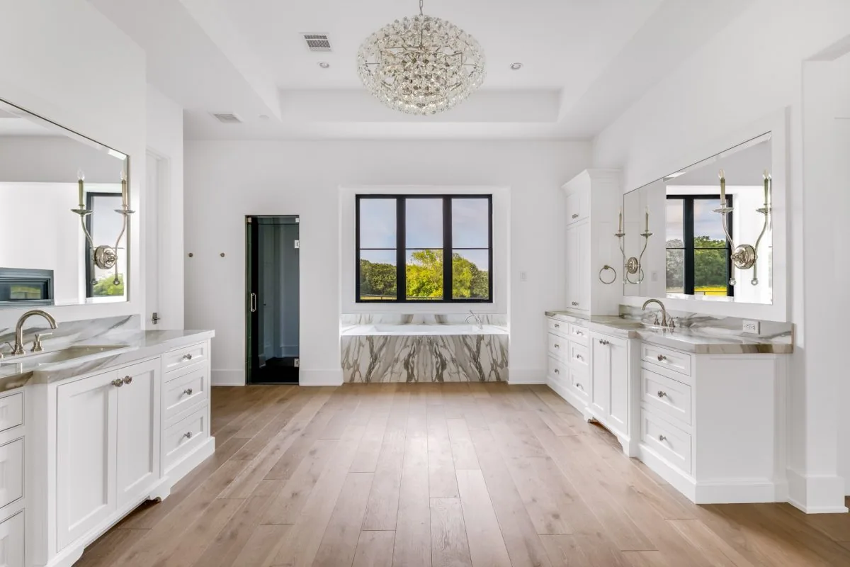 Bathroom in Hill Country Estate features dual vanities, a marble tub surround, and a large window.