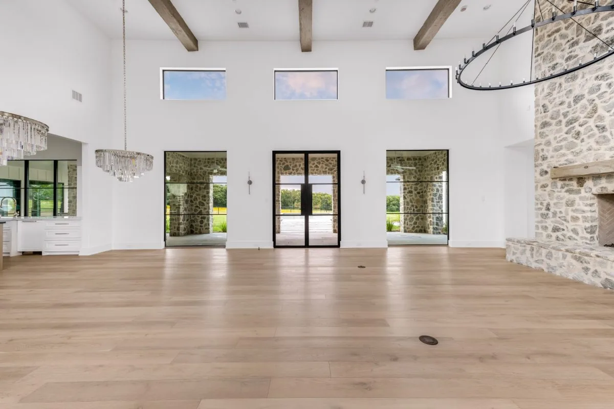 The Hill Country Estate living room features a stone fireplace, clerestory windows, and exposed wood ceiling beams.