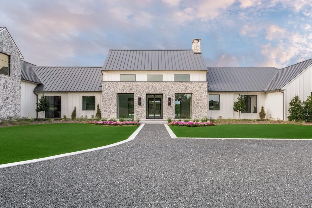 Hill Country Estate with stone chimney, metal roof, and gravel driveway, featuring a symmetrical front entry.