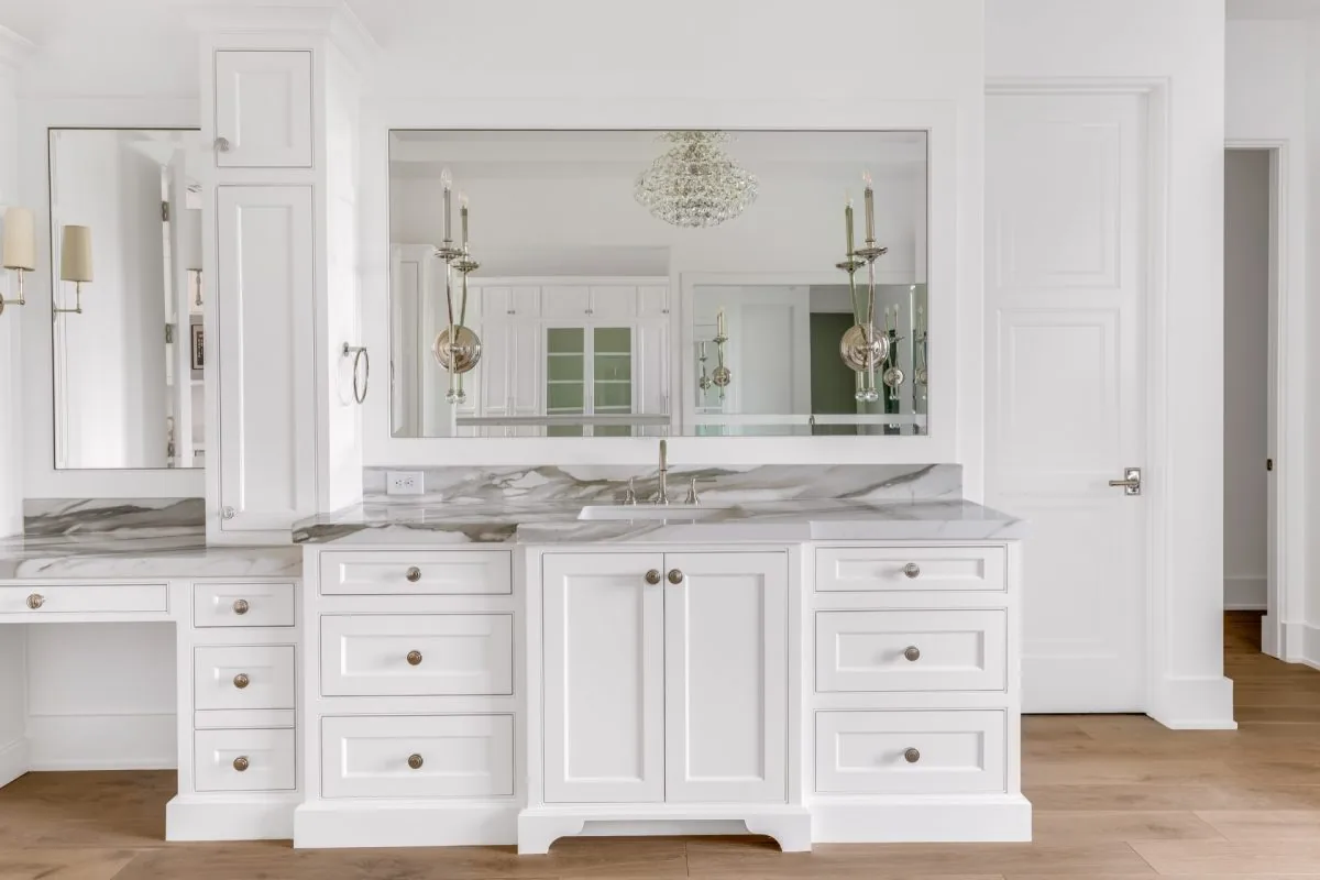 This bathroom features a white vanity with marble countertop and twin wall sconces reflected in a wide mirror.