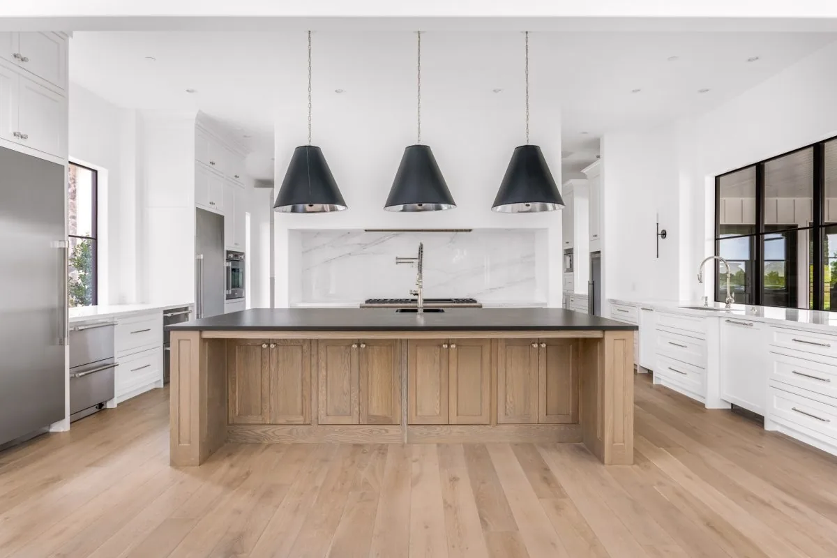 This kitchen features a wooden island with black top and three black pendant lights above, surrounded by white cabinetry and stainless steel appliances.