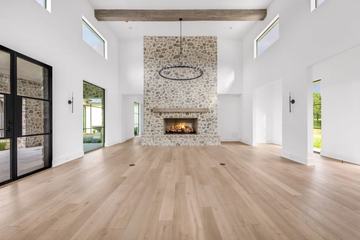 Living room in Hill Country Estate with stone fireplace, high ceilings, and light hardwood floors.
