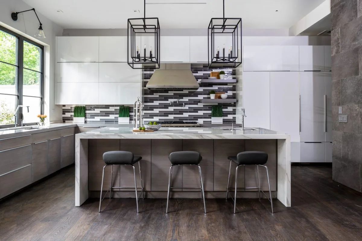Modern kitchen features a large marble island with seating, black window frames, and pendant lighting above the island.