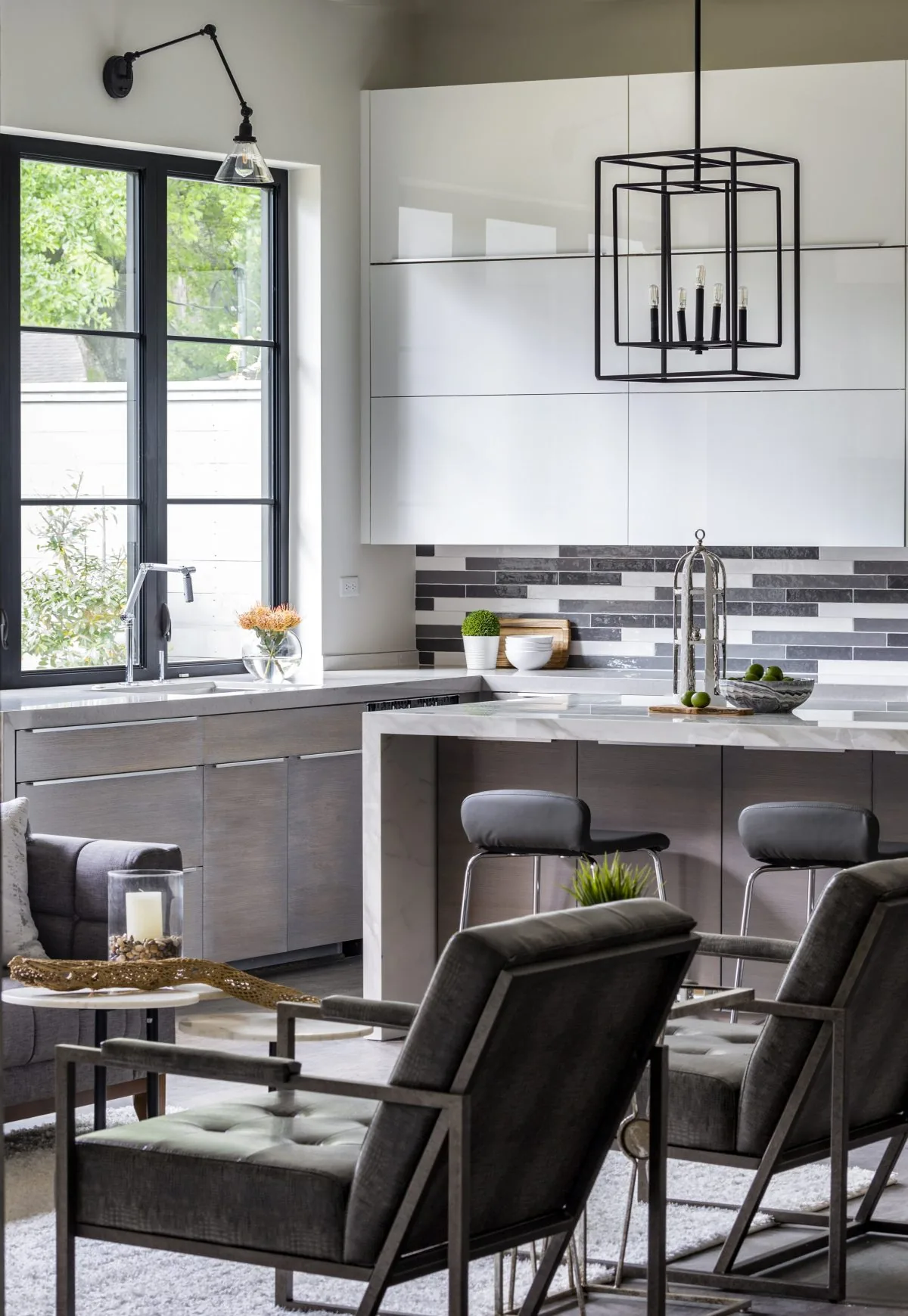 The modern kitchen features black-framed windows, a marble island, and a geometric pendant light above seating.