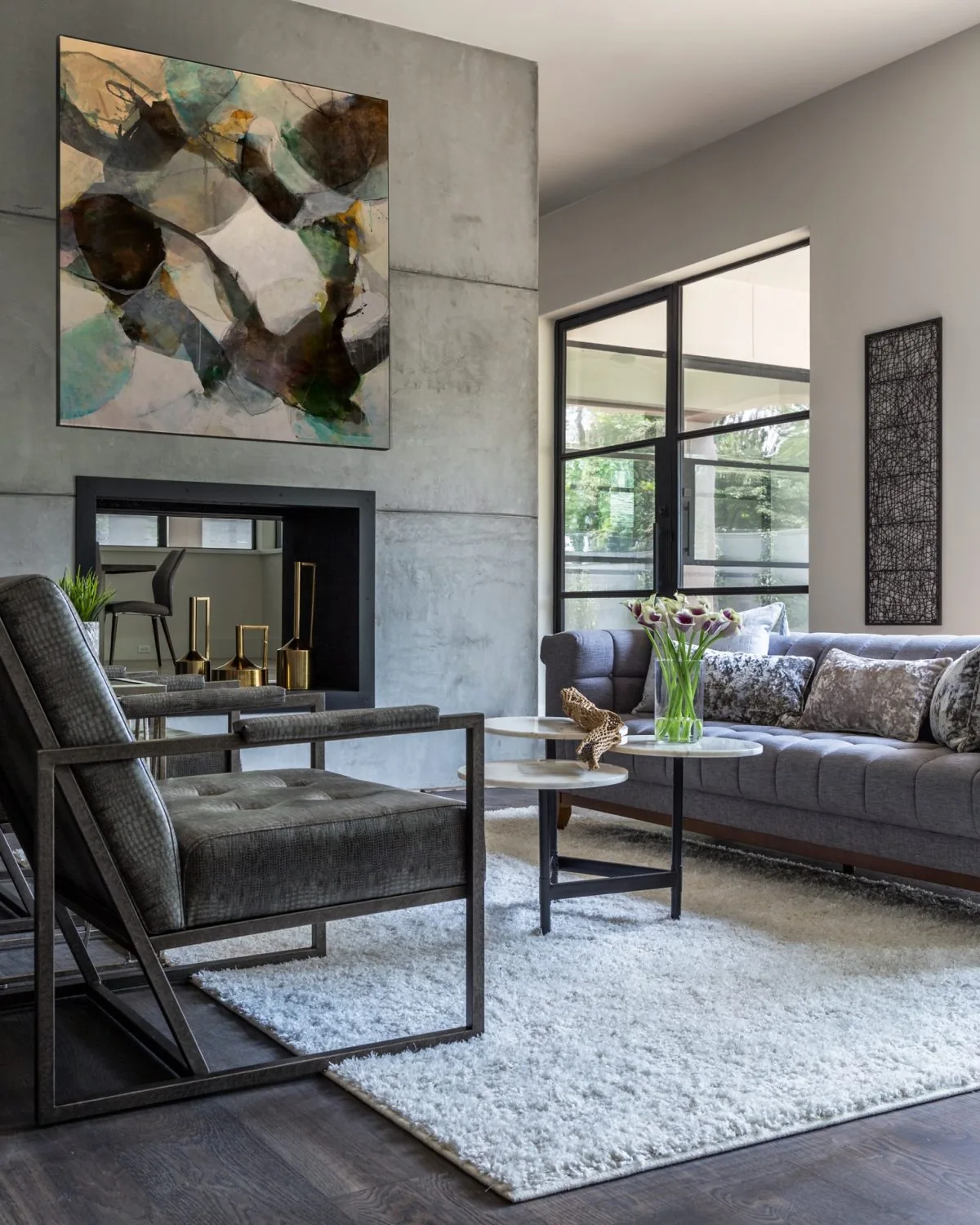 Living room featuring a textured concrete wall, gray upholstered sofa, abstract art, and a large window with black frames.