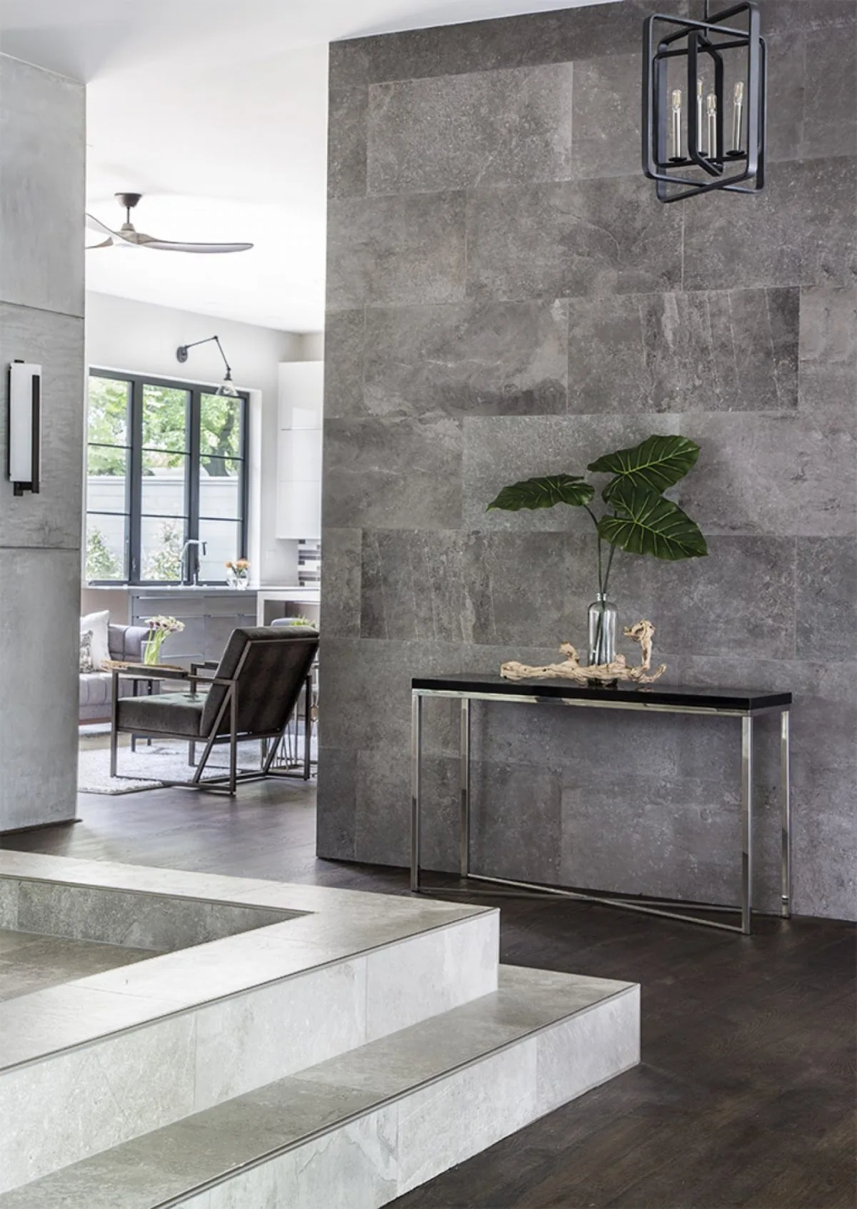 Modern entry foyer features a textured stone tile wall and sleek console table accented with a green leaf arrangement.