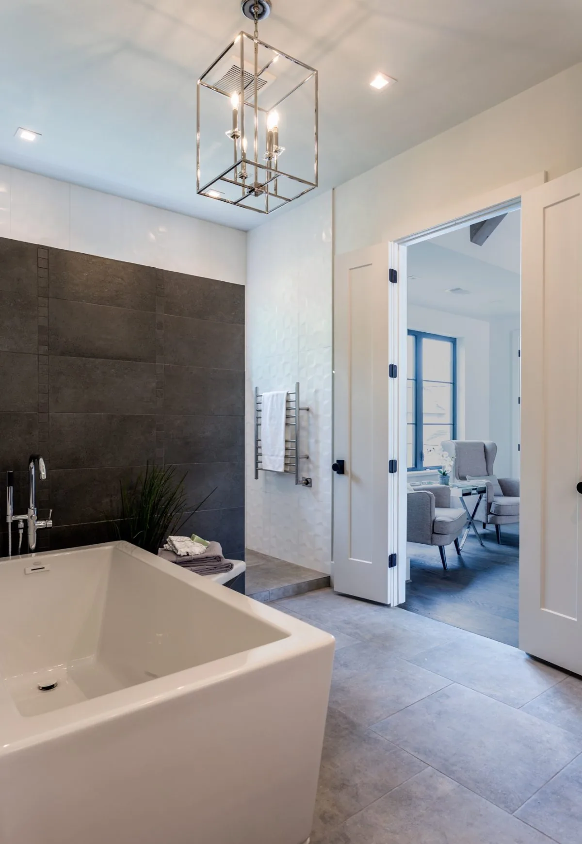 Bathroom with a deep soaking tub, geometric chandelier, dark tile accent wall, and white textured wall detail