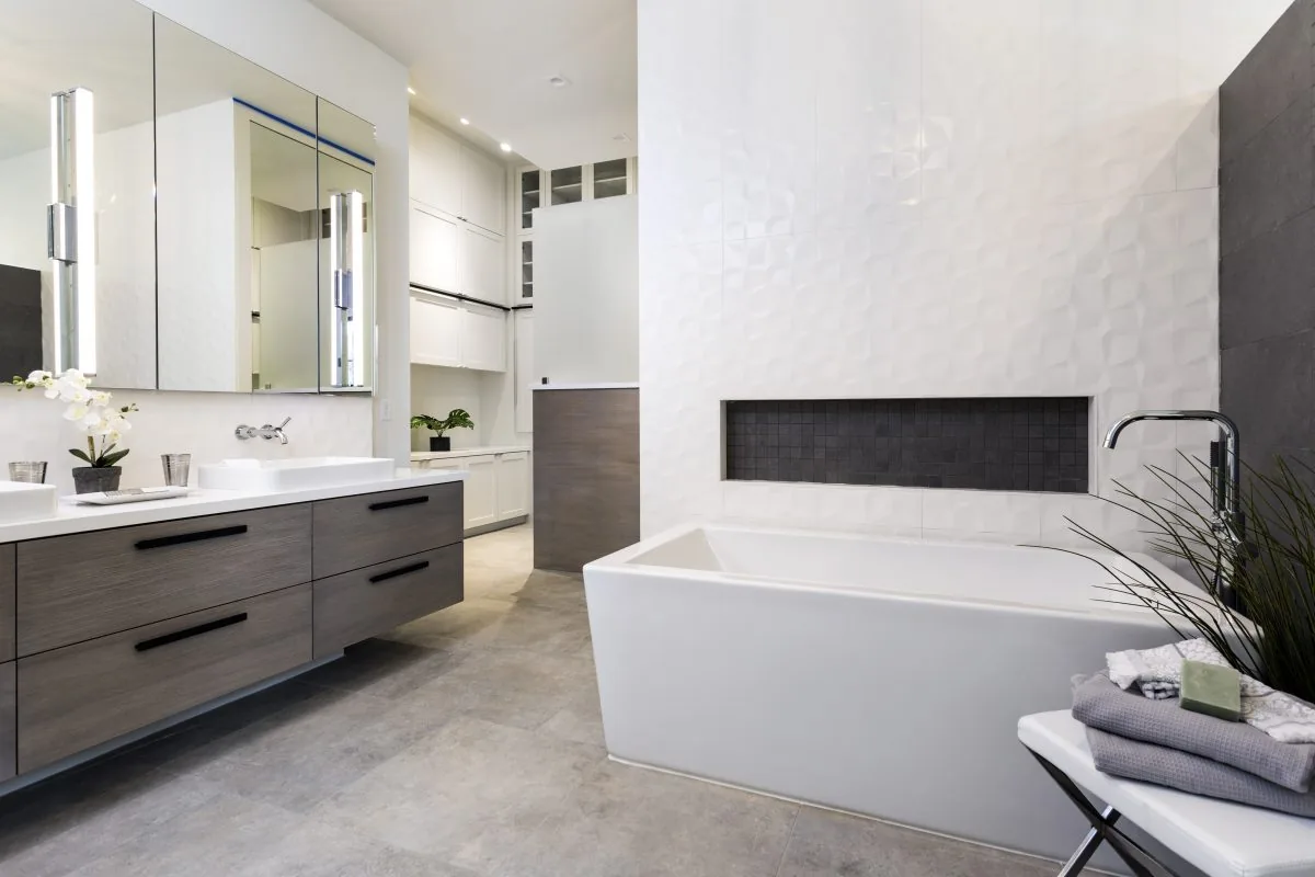 Bathroom with grey wood floating vanity, double undermount sinks, and a deep soaking tub with a textured tile accent wall.