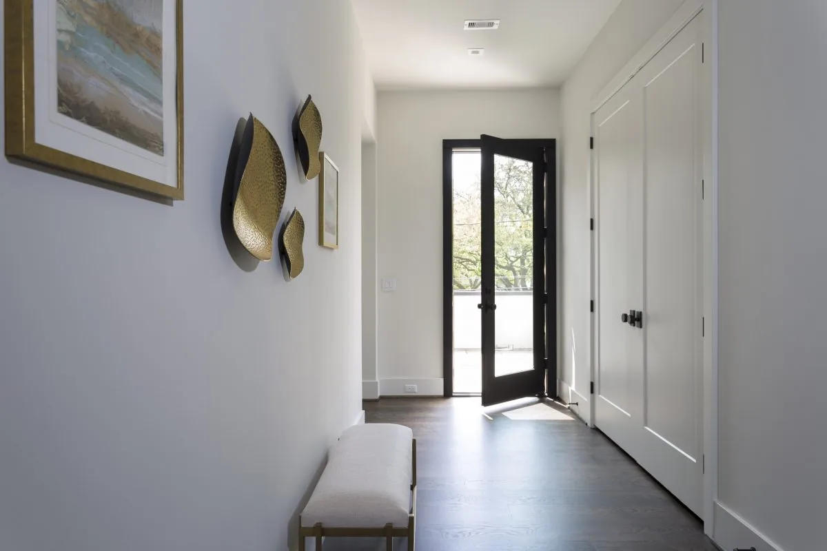 Entry hallway featuring a black framed glass door, white walls, wooden floors, and a bench with metal wall accents.