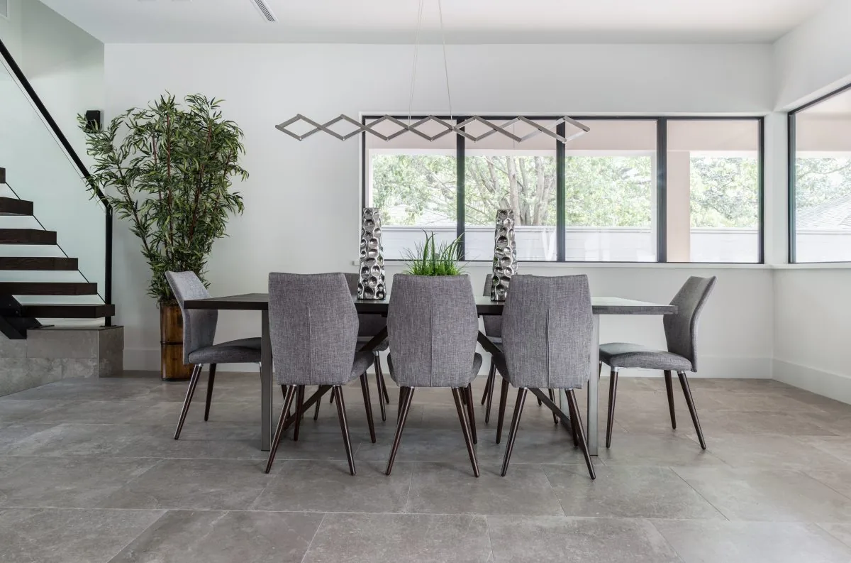 A modern dining room featuring gray upholstered chairs and a geometric pendant light above a rectangular dining table.