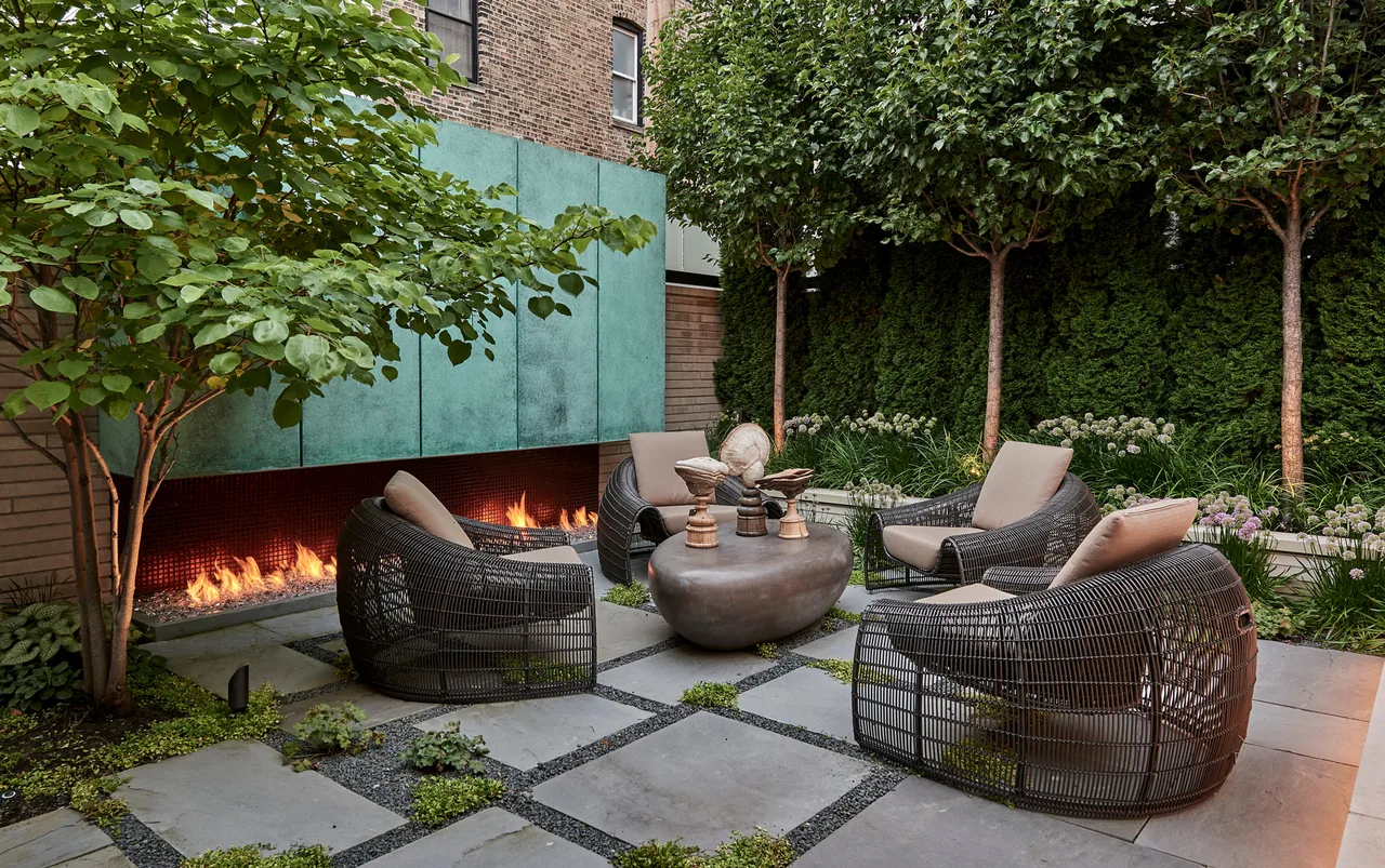 Outdoor living patio with woven chairs, stone table, and long gas fireplace at Lakewood Residence, Chicago.